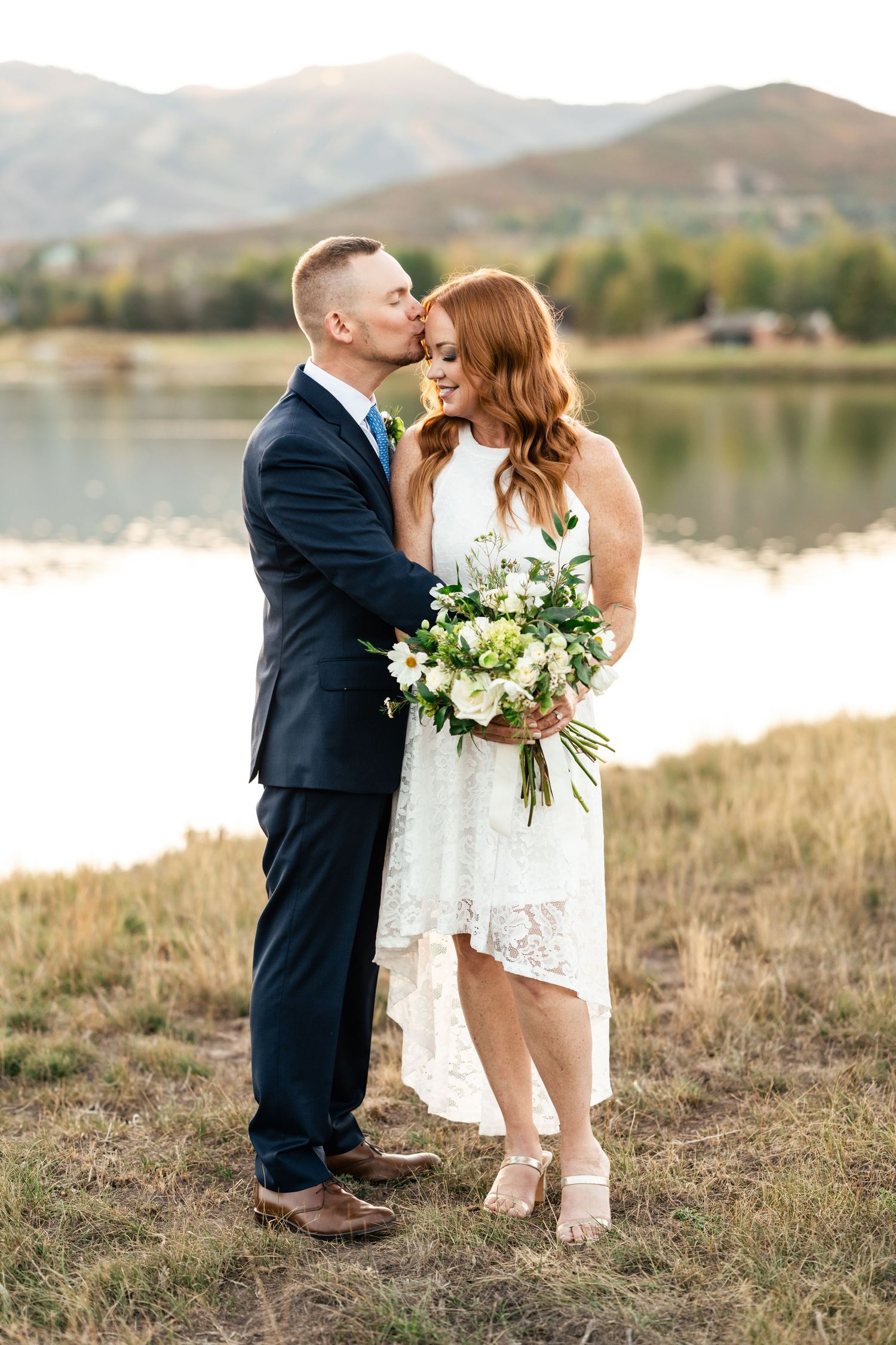 Romantic wedding photos taken at sunset by a lake with mountains in the background.
