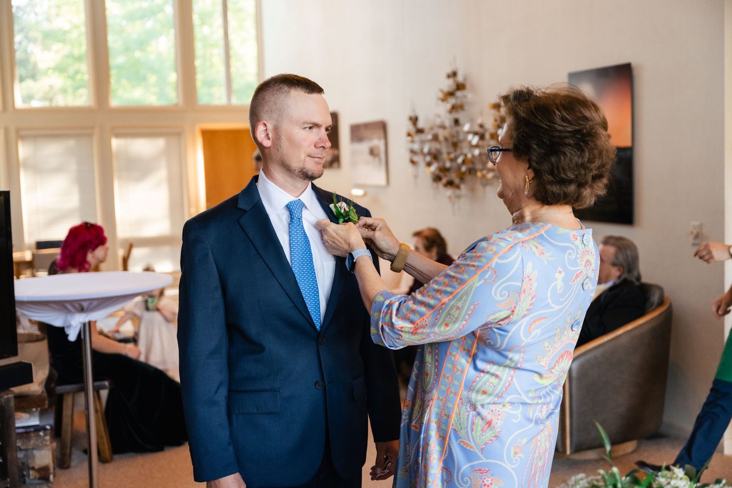 Wedding preparation scene showing a boutonniere being pinned on a navy blue suit.