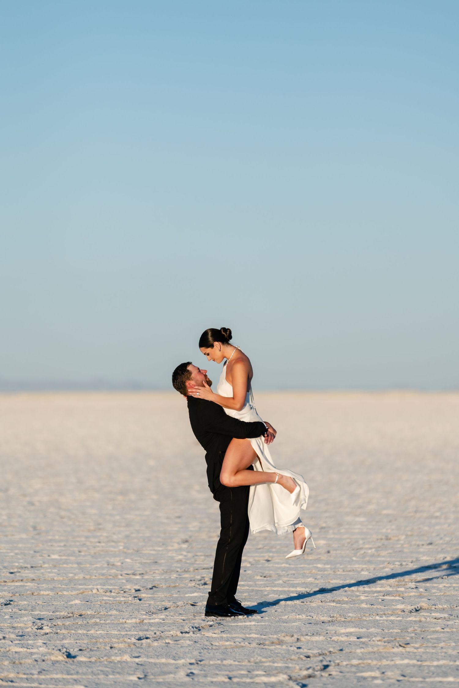 Salt Flats Photographer. Romantic couple embrace on salt flats with clear blue sky background.