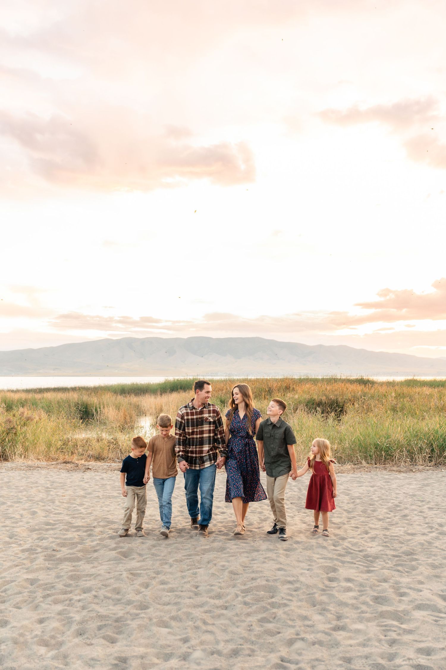 A group of people walking together on a sandy beach at sunset with mountains visible in the background.