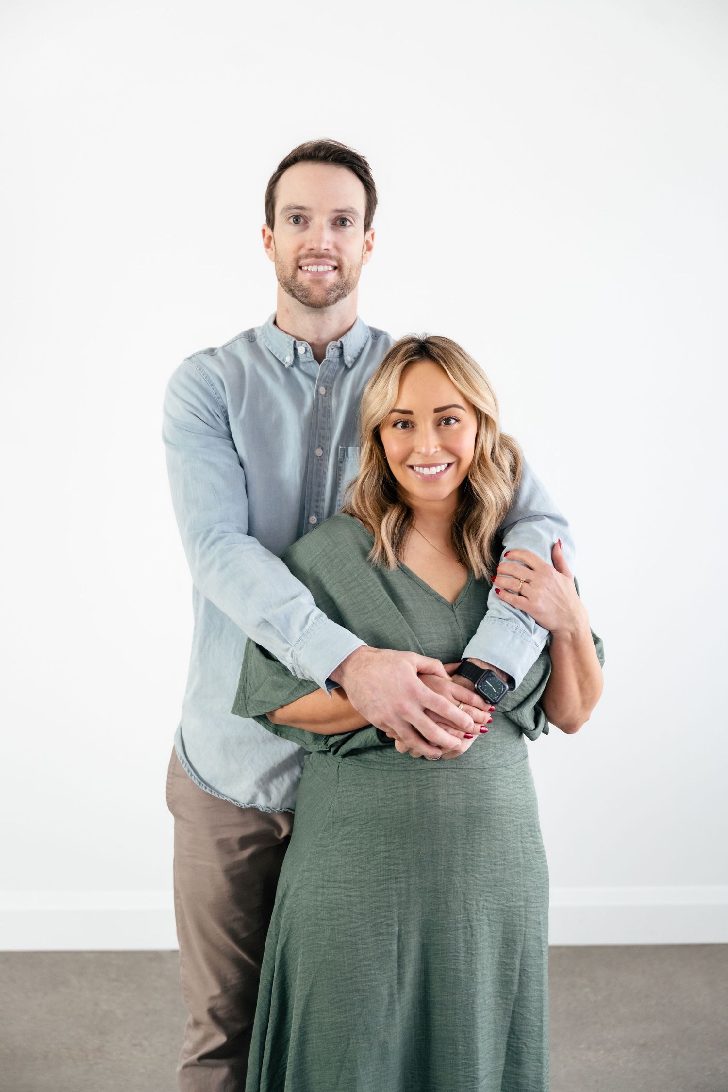 A couple in casual attire embraces while standing against a white backdrop in a progression of three poses.