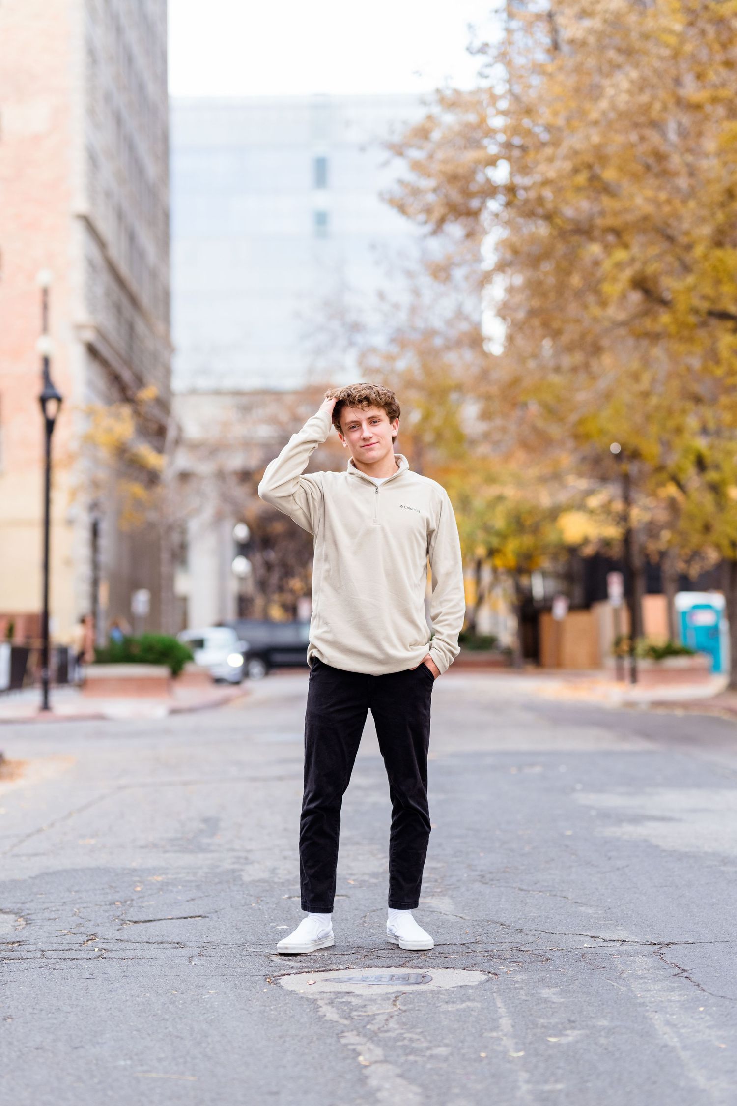 Someone stands on an autumn city street wearing a cream colored sweater and black pants with white sneakers.