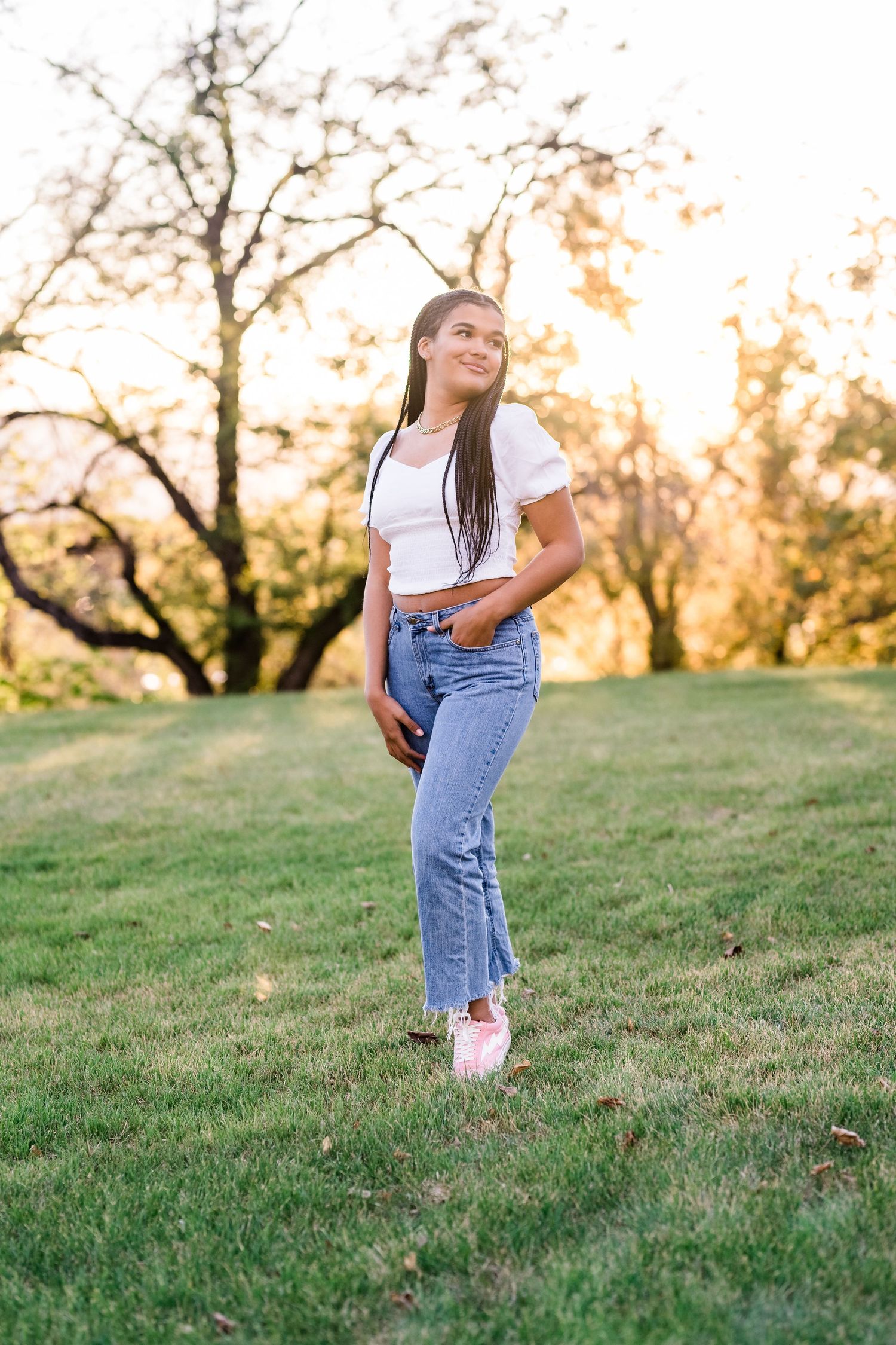 A child in denim overalls stands on a grassy hillside during golden hour sunset.
