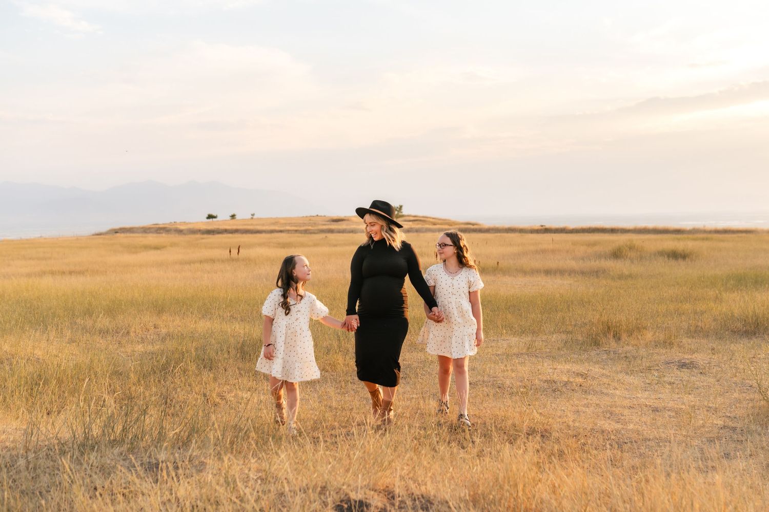 Three people walk together through a golden field at sunset with warm lighting and long shadows cast across the landscape.