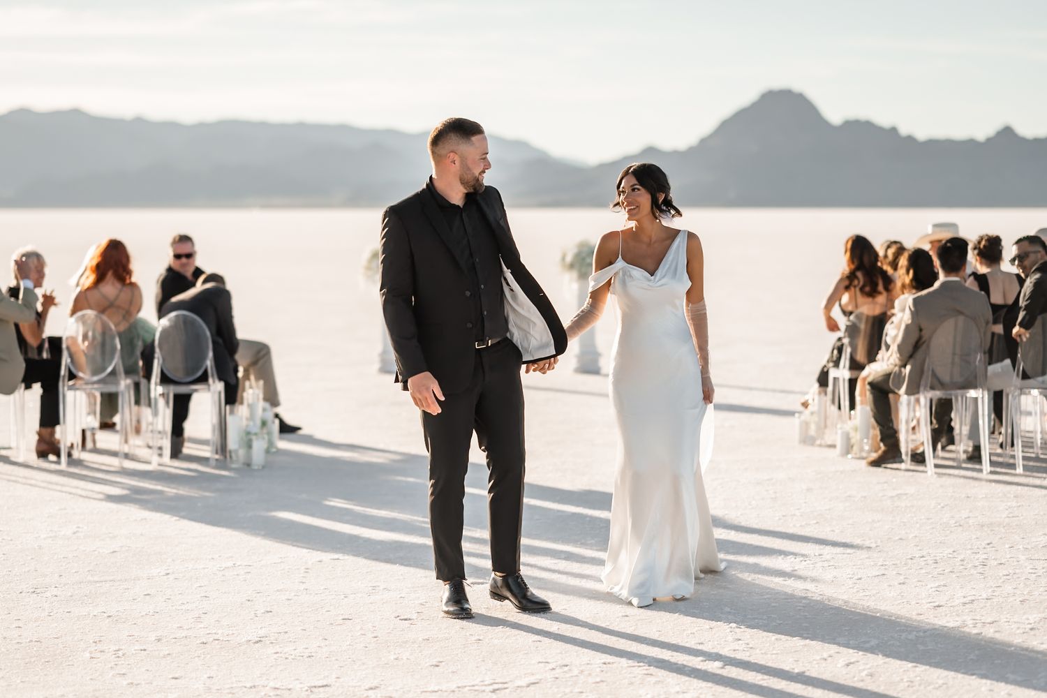 Wedding guests and ceremony setup on expansive white salt flats under bright sky.