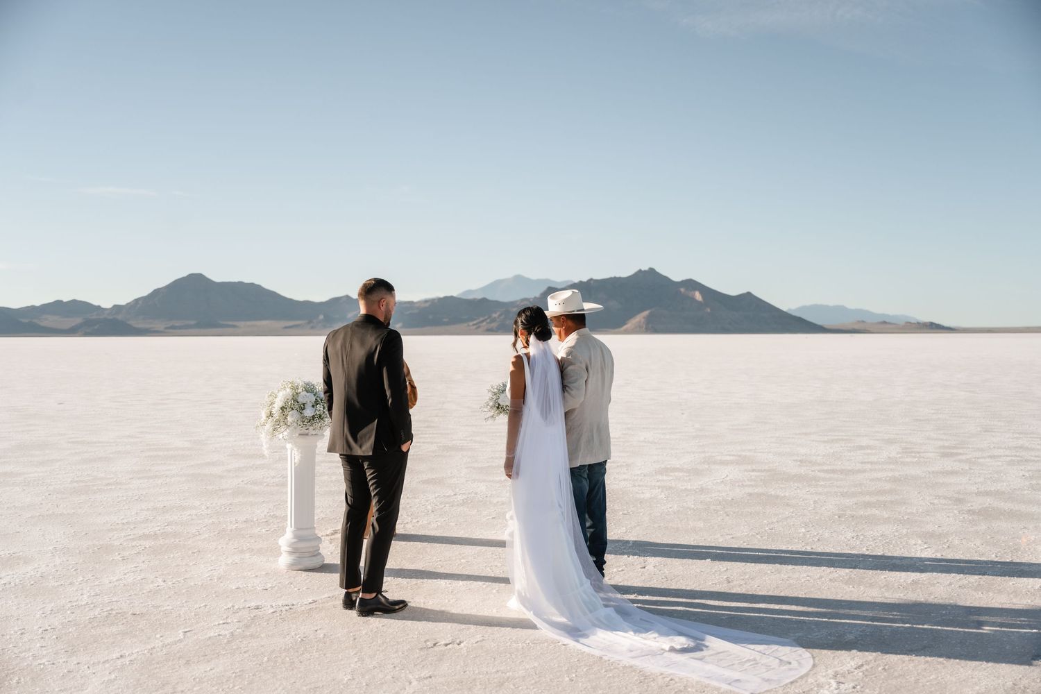 Wedding couple walks hand in hand across the pristine white salt flats with mountains visible in the distance.