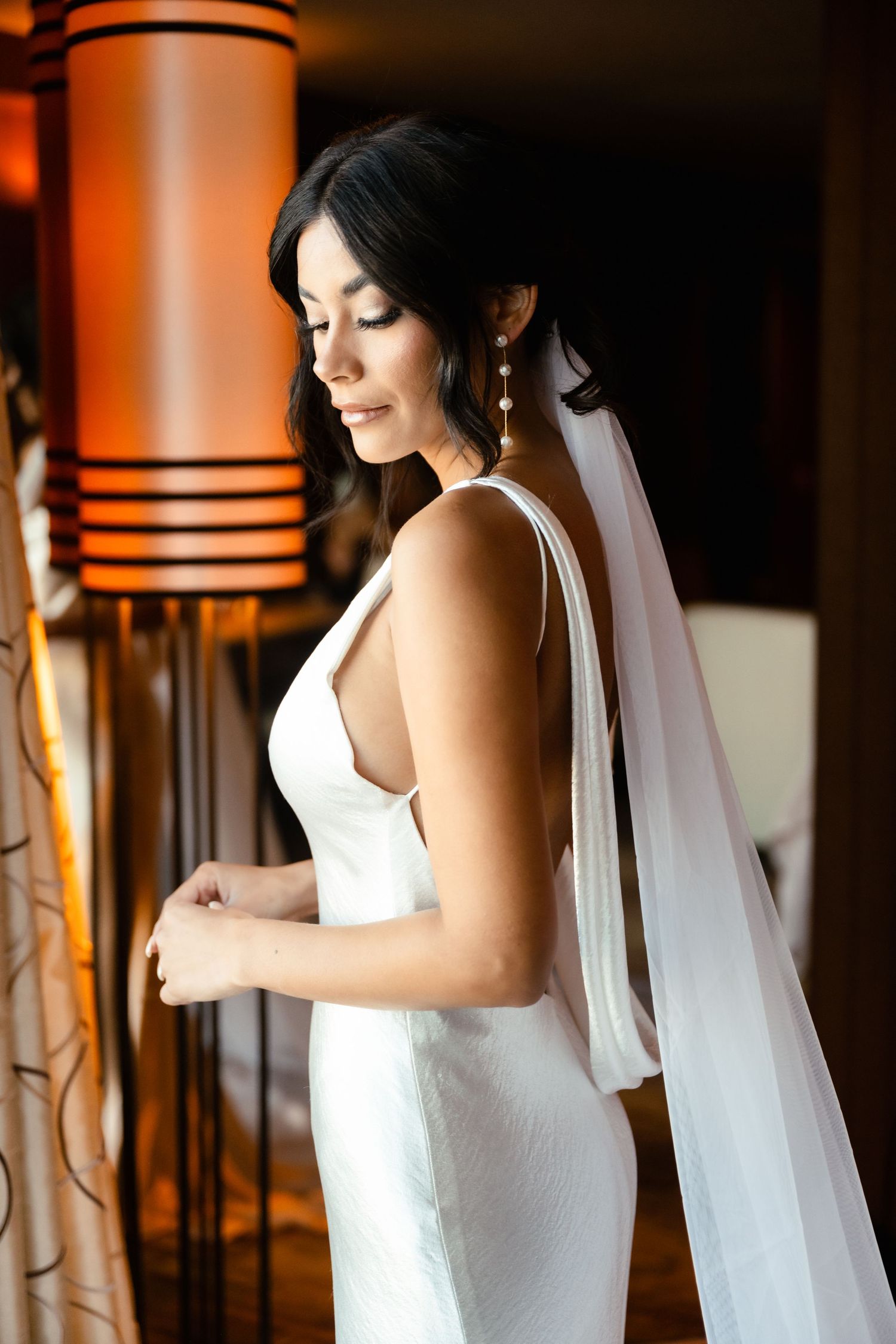 Bride getting ready in an elegant room with warm lighting and cylindrical lamp shades.