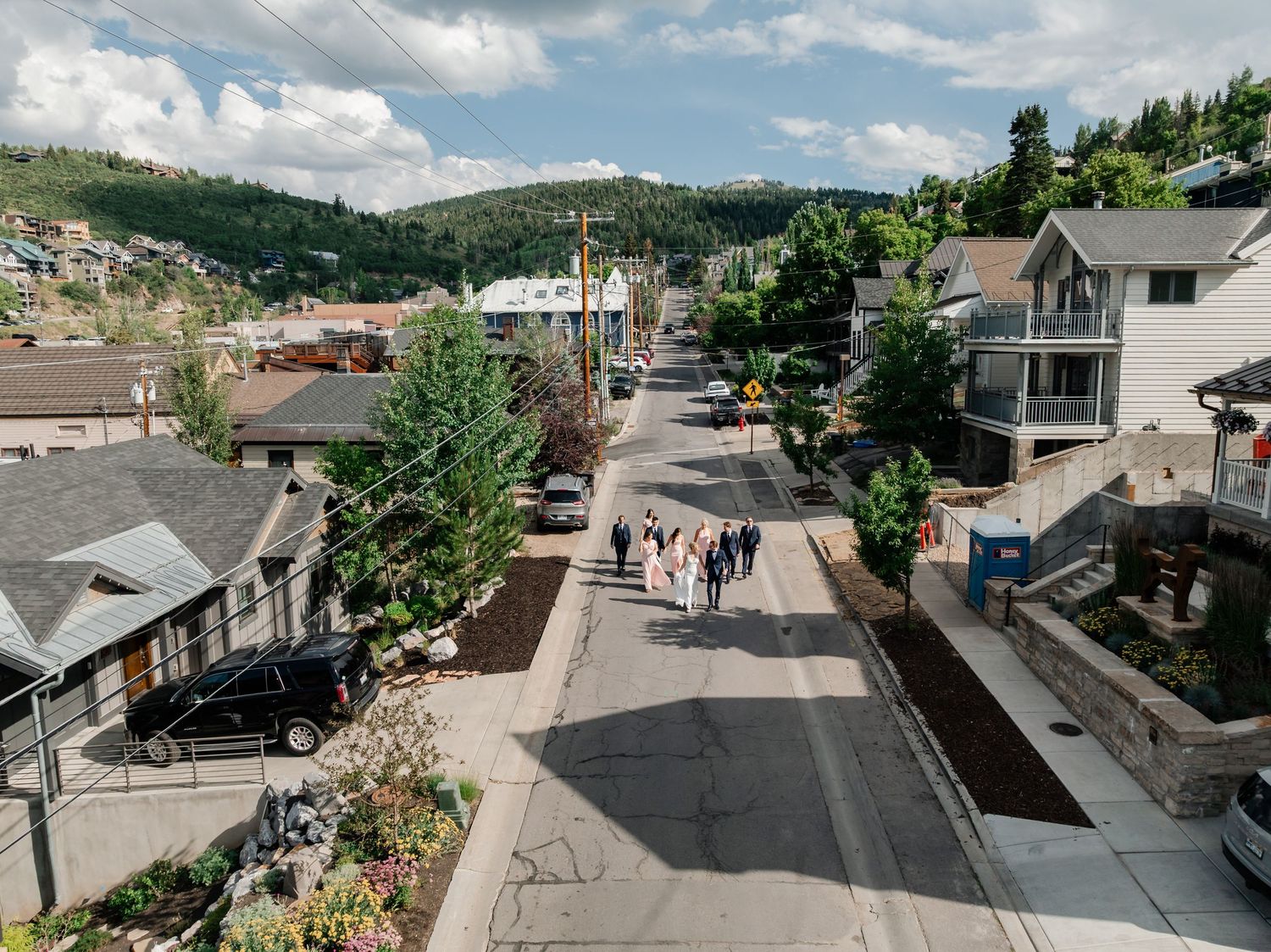 A panoramic view of a residential neighborhood with houses nestled on hillsides under blue skies and white clouds.
