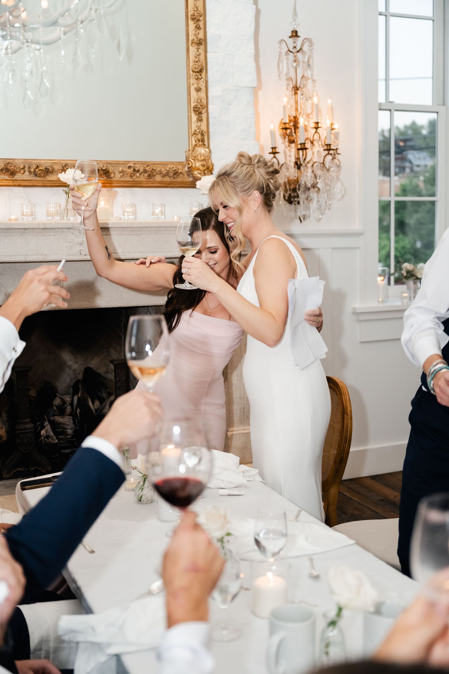 Wedding reception guests raising glasses for a celebratory toast in an elegant white room.