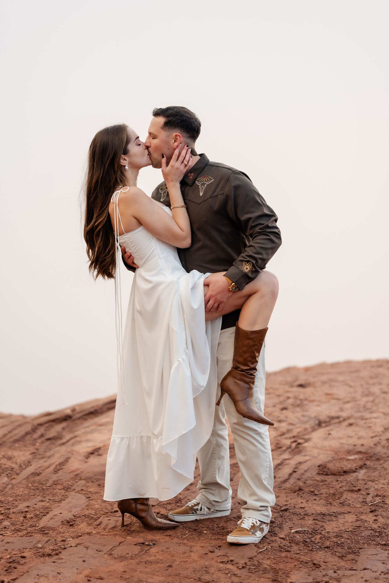 A romantic couple shares a passionate kiss on red rocks during a desert photoshoot.