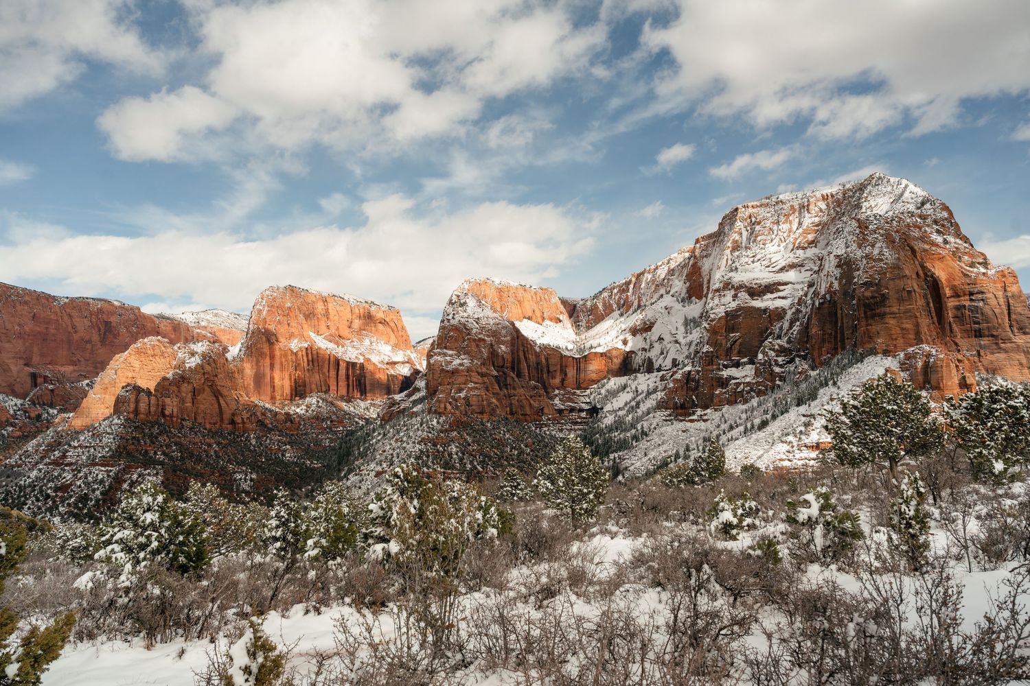 Panoramic view of snow-dusted red sandstone cliffs against blue sky in Zion National Park.