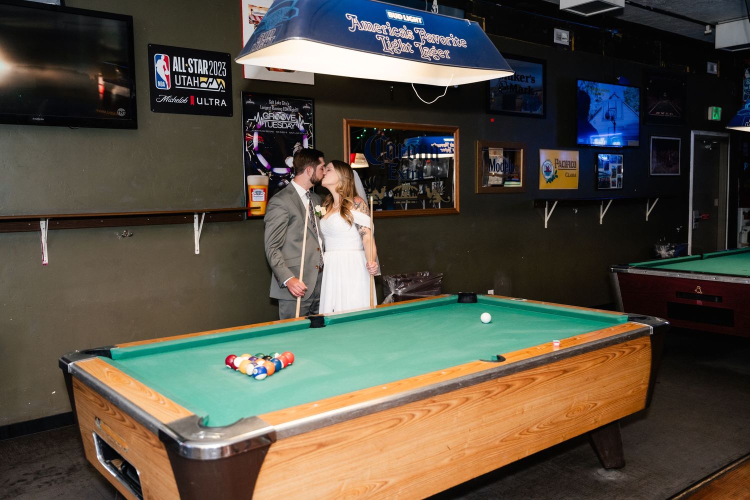 Players enjoying a game of pool at a dimly lit bar with multiple pool tables visible in the background.