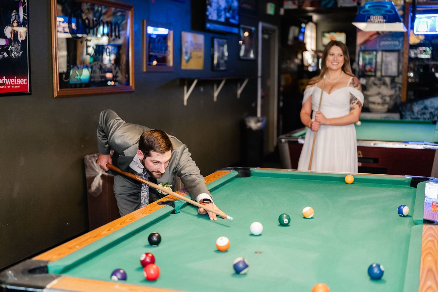 A couple plays pool in a dimly lit bar with sports memorabilia on the walls.