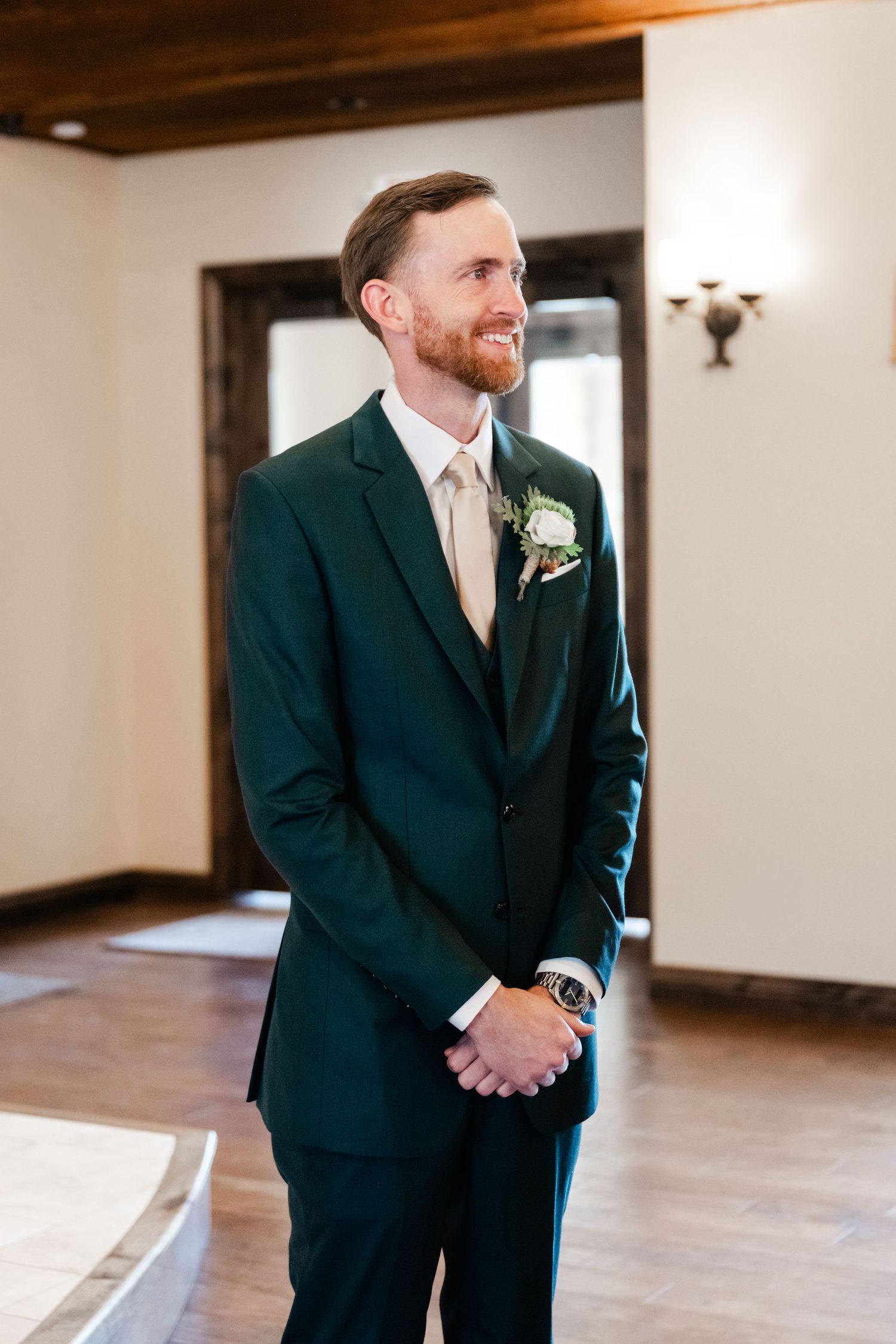 A groom in a dark suit and tie shows emotion during a wedding ceremony in an elegant indoor venue.