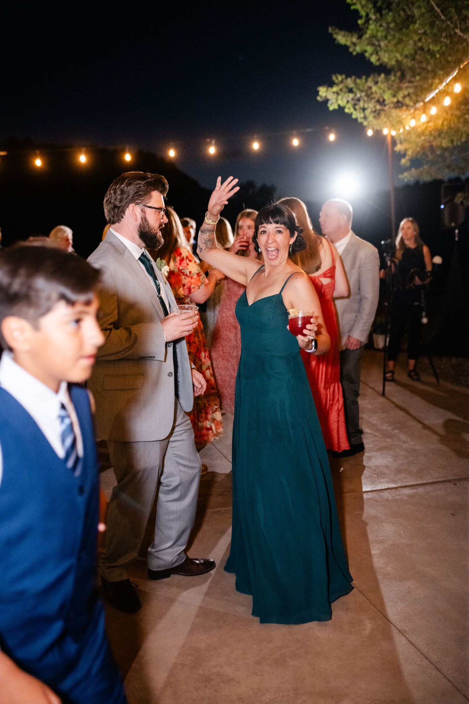 Wedding guests dance and celebrate on an outdoor patio under evening string lights.
