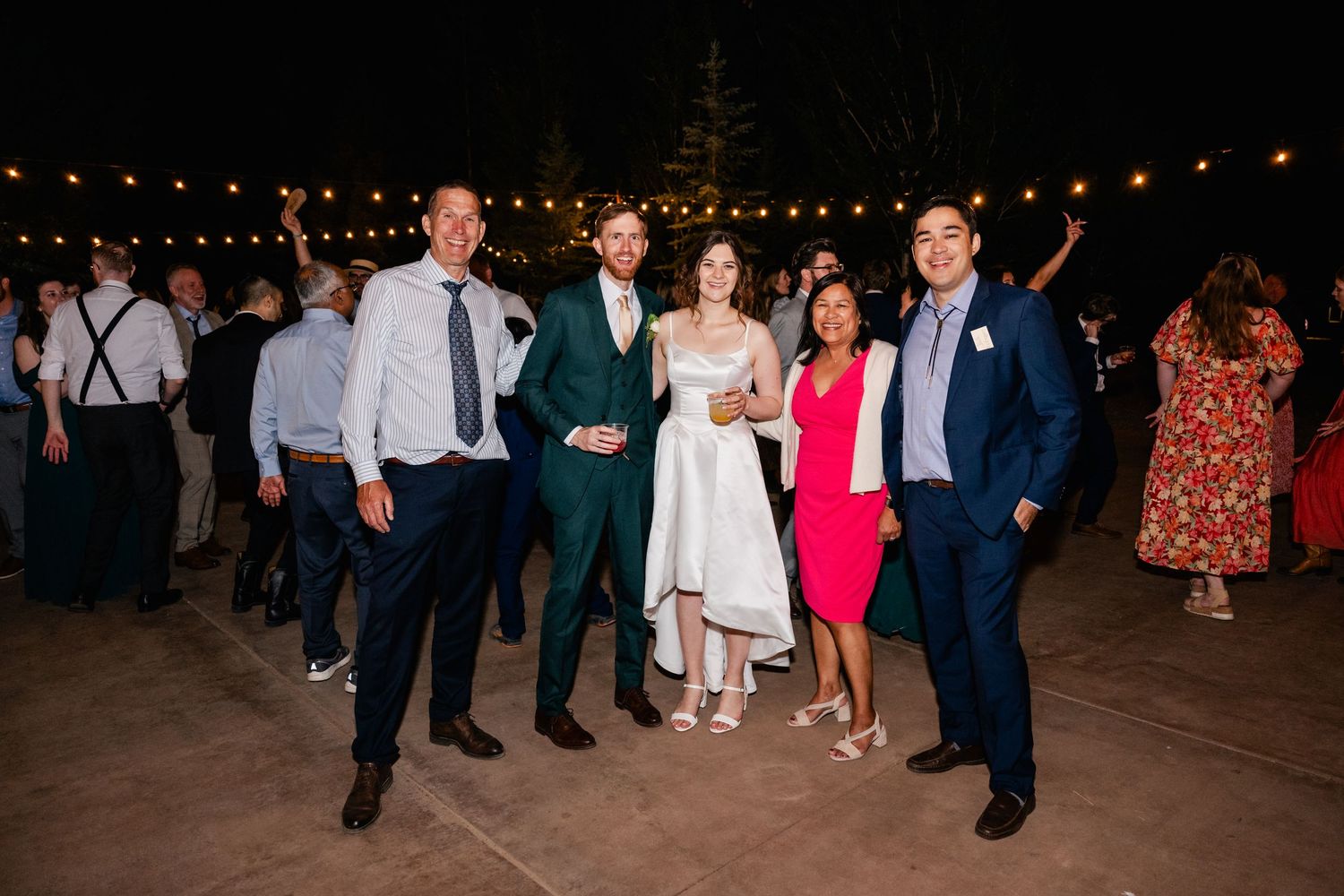 Festive outdoor reception with string lights illuminating people dancing and mingling.