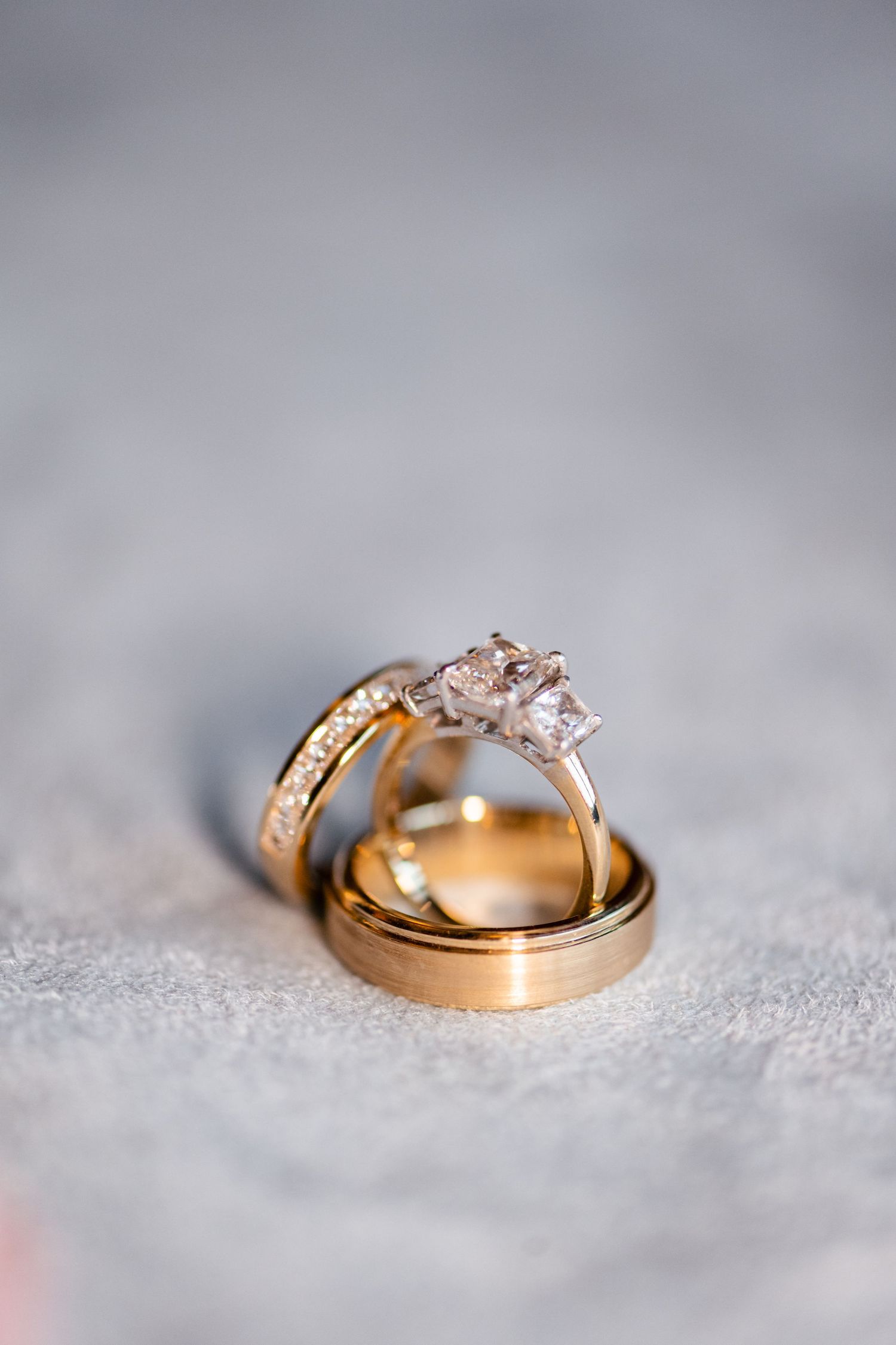 Gold wedding rings with diamonds photographed in close-up detail on a textured gray surface.