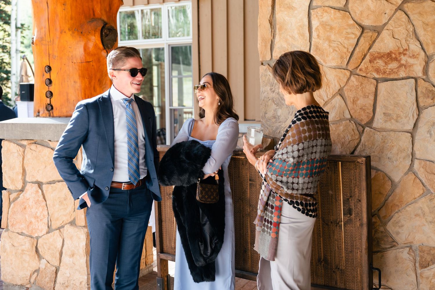 Wedding party stands in front of rustic stone wall during outdoor ceremony.