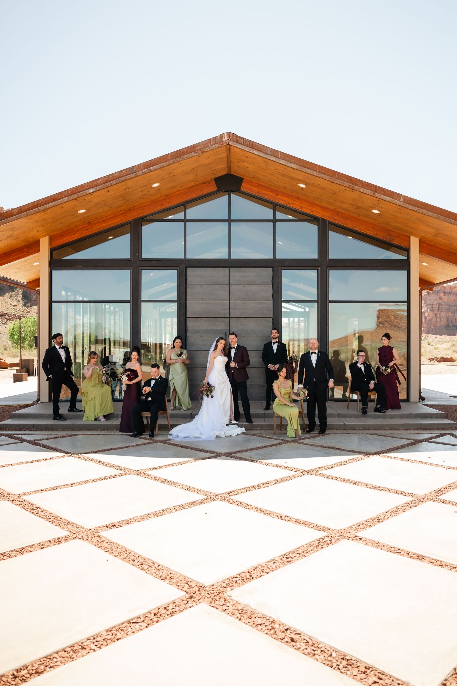 The Red Earth Venue in Moab. Wedding party poses in front of a modern desert venue with large glass windows and wood-beam architecture.