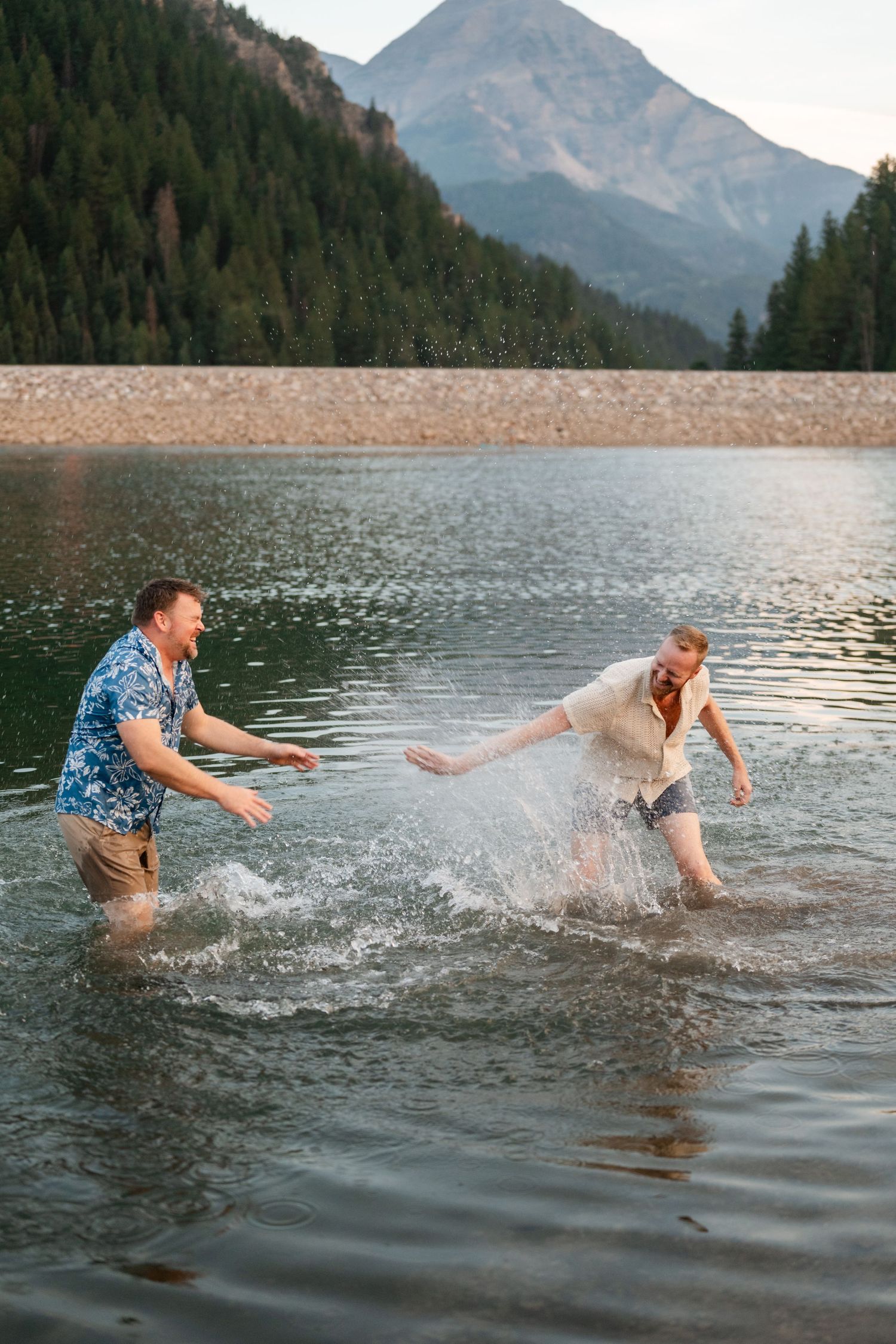 Couple having a water fight at Tibble Fork Reservoir. Two men laughing and splashing water in a mountain lake surrounded by pine trees.