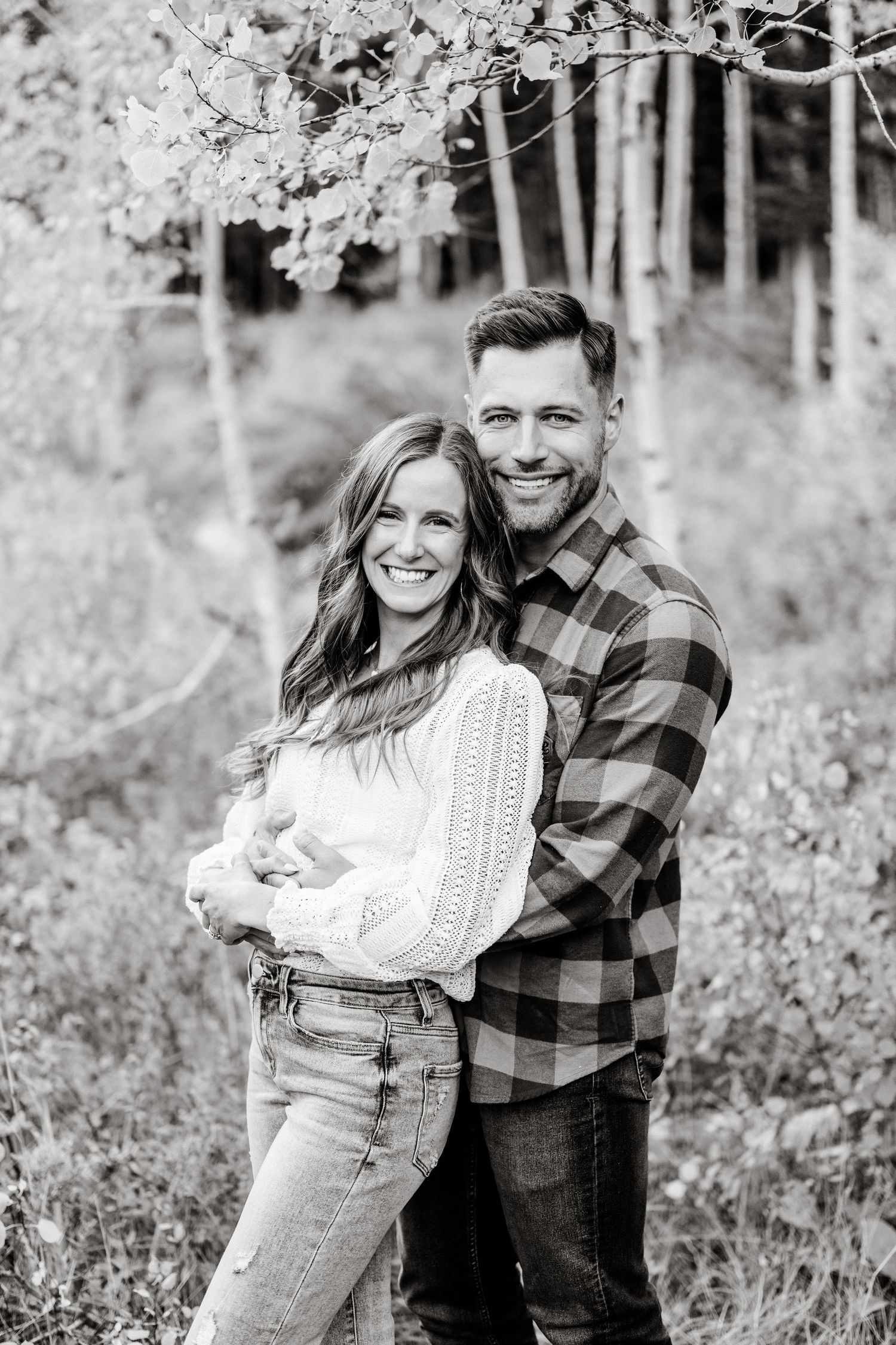 A loving couple in coordinated casual wear embraces while posing for a black and white portrait in nature.