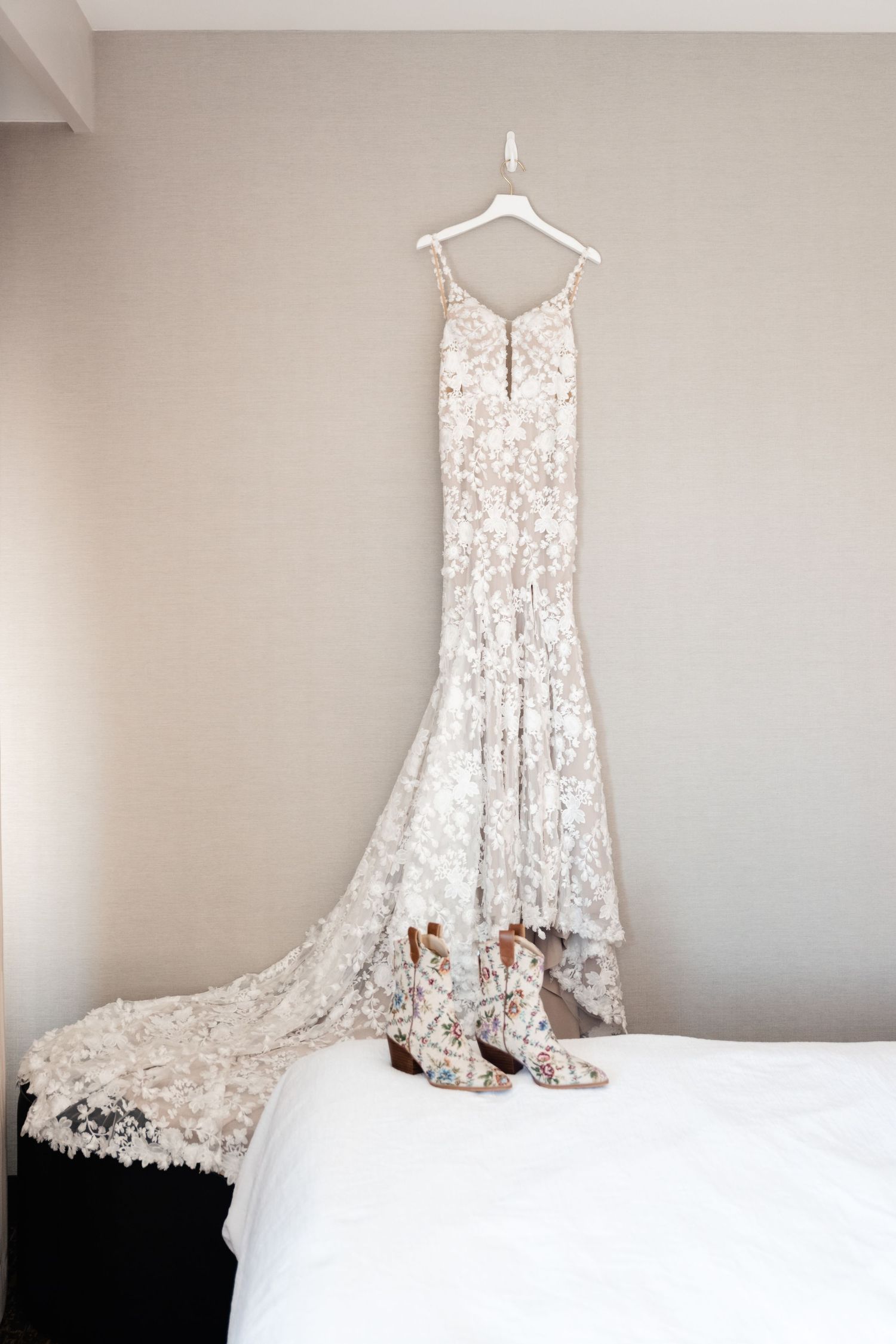 Elegant lace wedding dress with train and matching heels displayed on a white hanger against neutral wall.