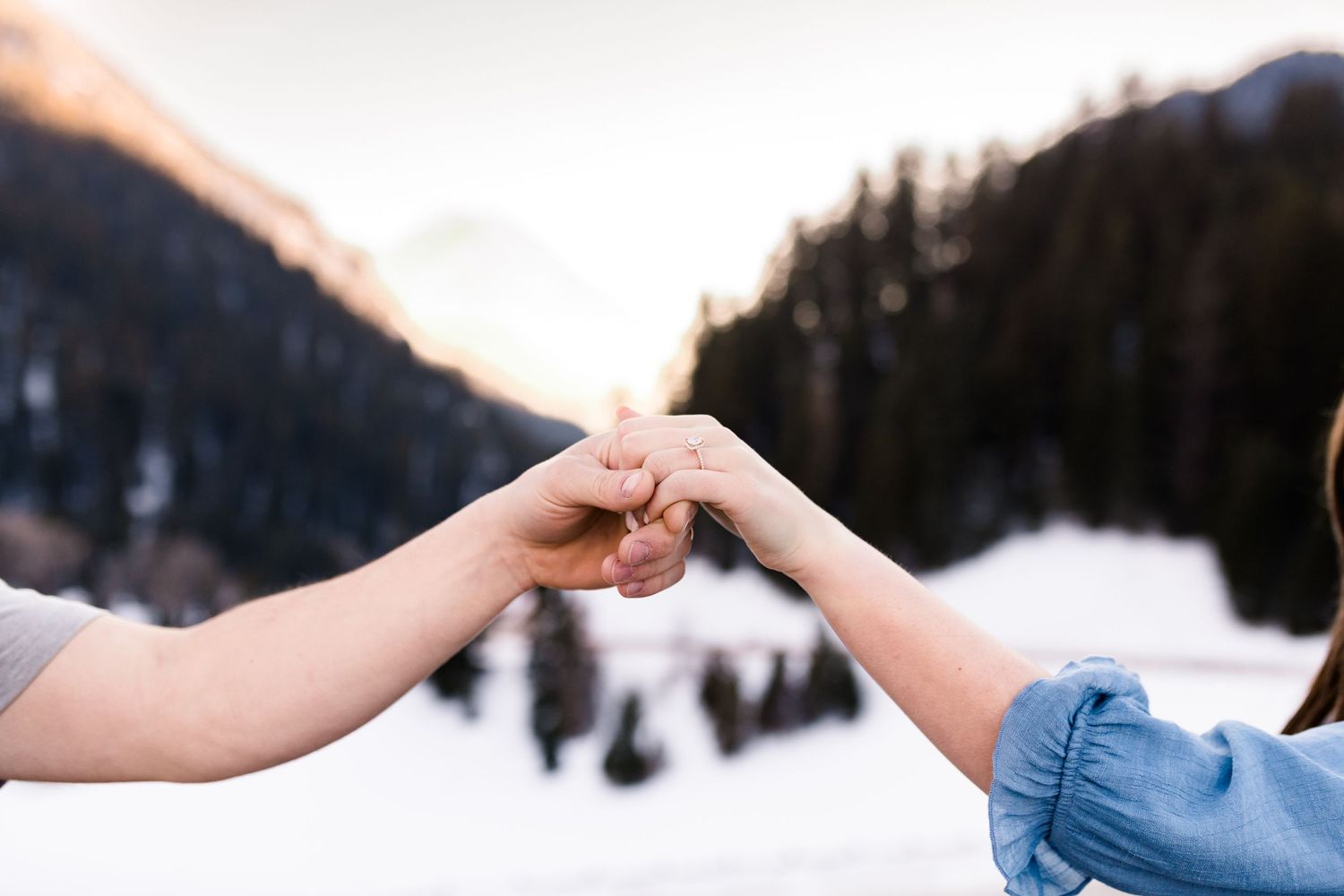 Two hands join together against a snowy mountain landscape at sunset.