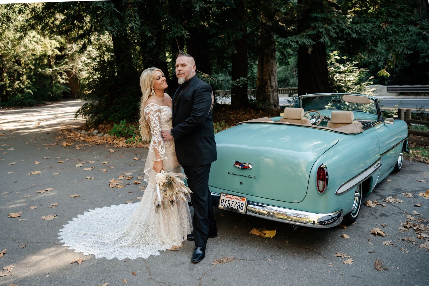 Classic turquoise convertible car parked under trees with autumn leaves.