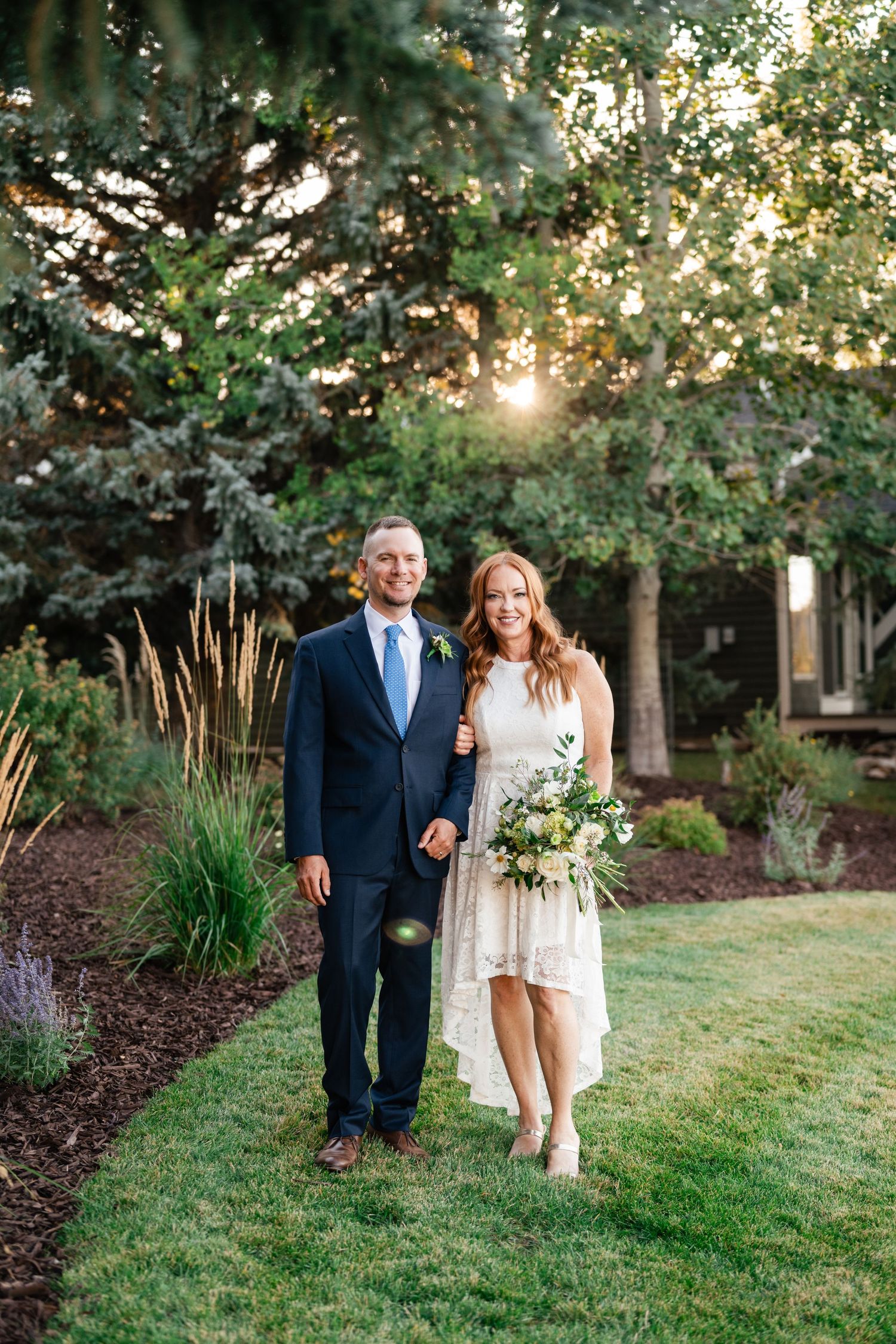 A couple poses together outdoors in a garden setting during golden hour.