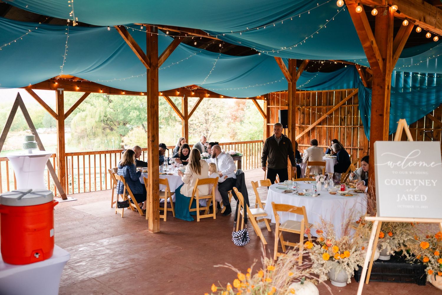 Rustic wooden pavilion decorated with string lights and white fabric for a wedding reception.