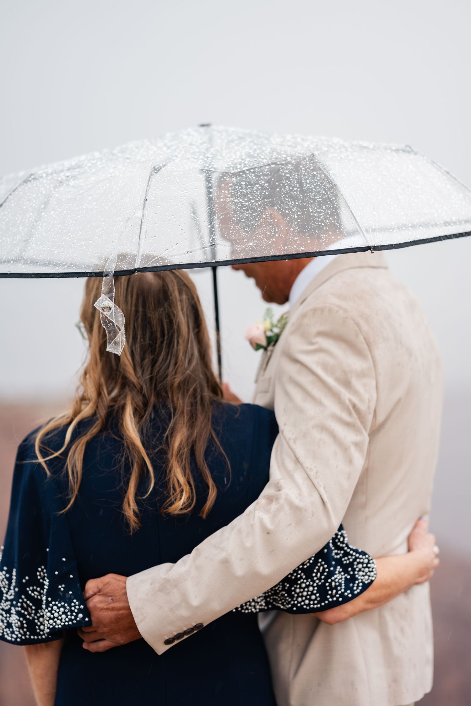 Wedding couple sharing intimate moment under clear umbrella on rainy day.