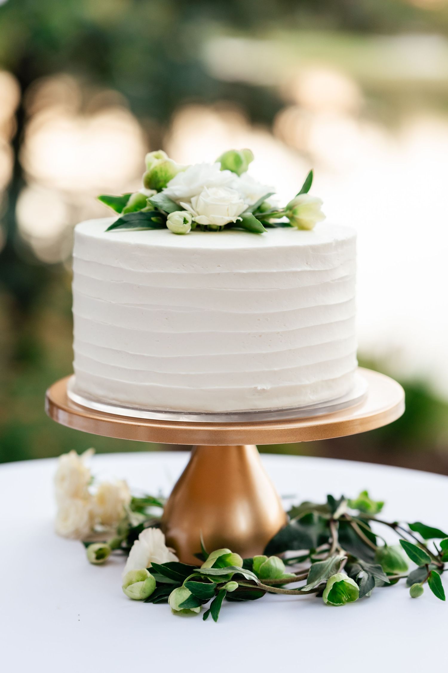White wedding cake with floral decorations displayed on a copper-colored cake stand.