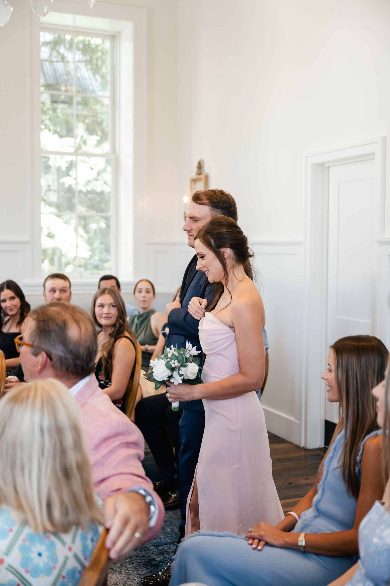 Wedding guests react with joy and excitement during an emotional ceremony moment in a bright white venue.