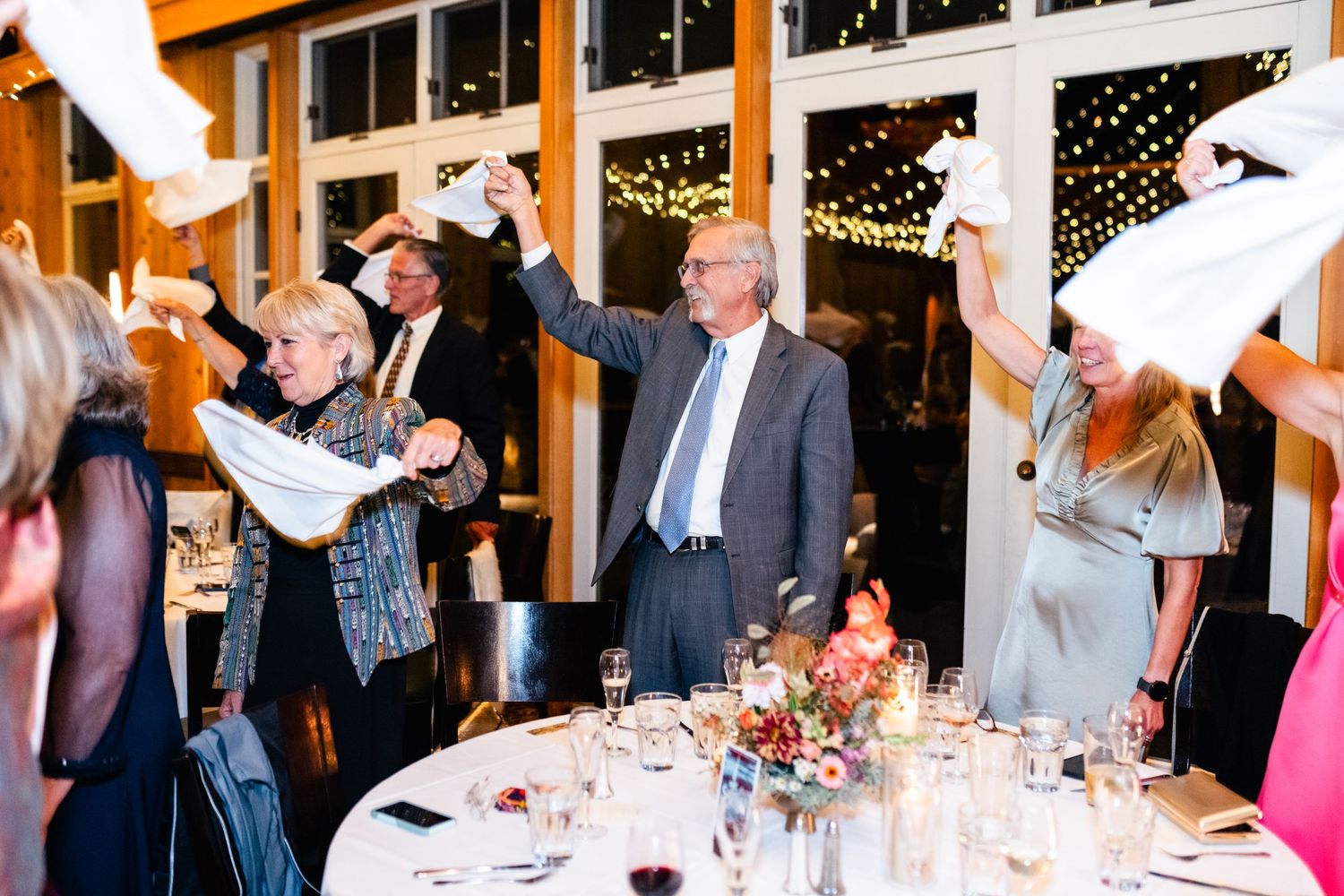 Wedding reception celebration with guests cheering and waving napkins.