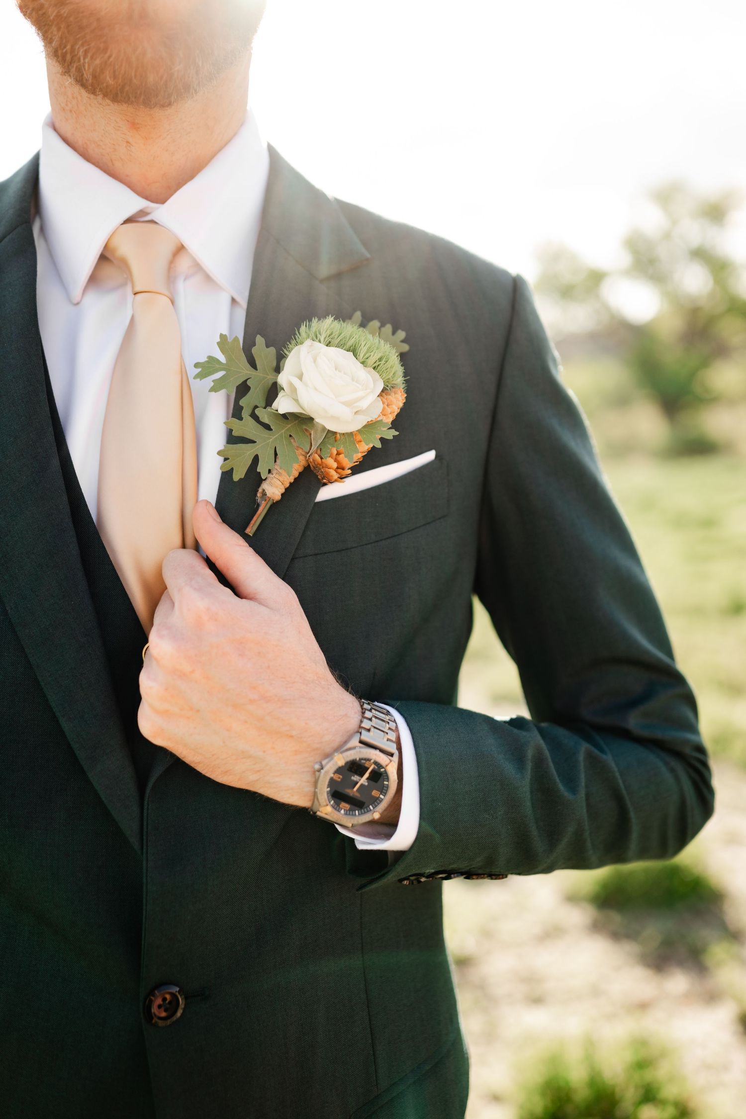 Close-up details of groom's formal attire with white boutonniere and champagne tie.