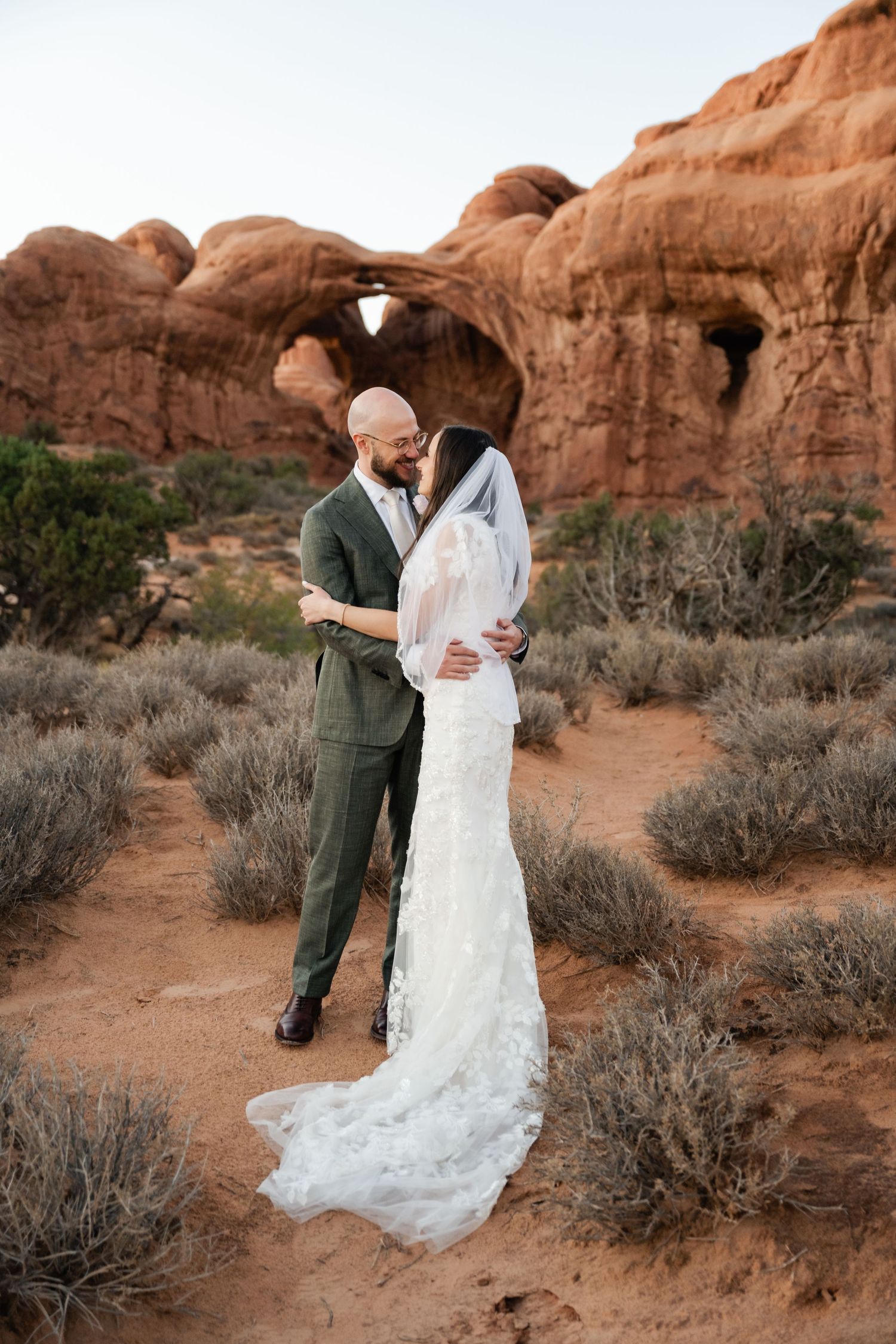 A couple shares an intimate dance moment among desert rock formations and sagebrush at sunset. Arches Wedding Photographer. Moab Wedding.