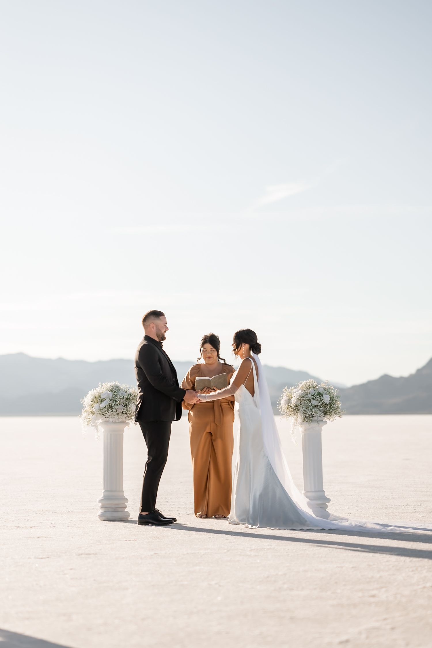 Intimate wedding ceremony on bright white salt flats with decorative columns and mountain views.