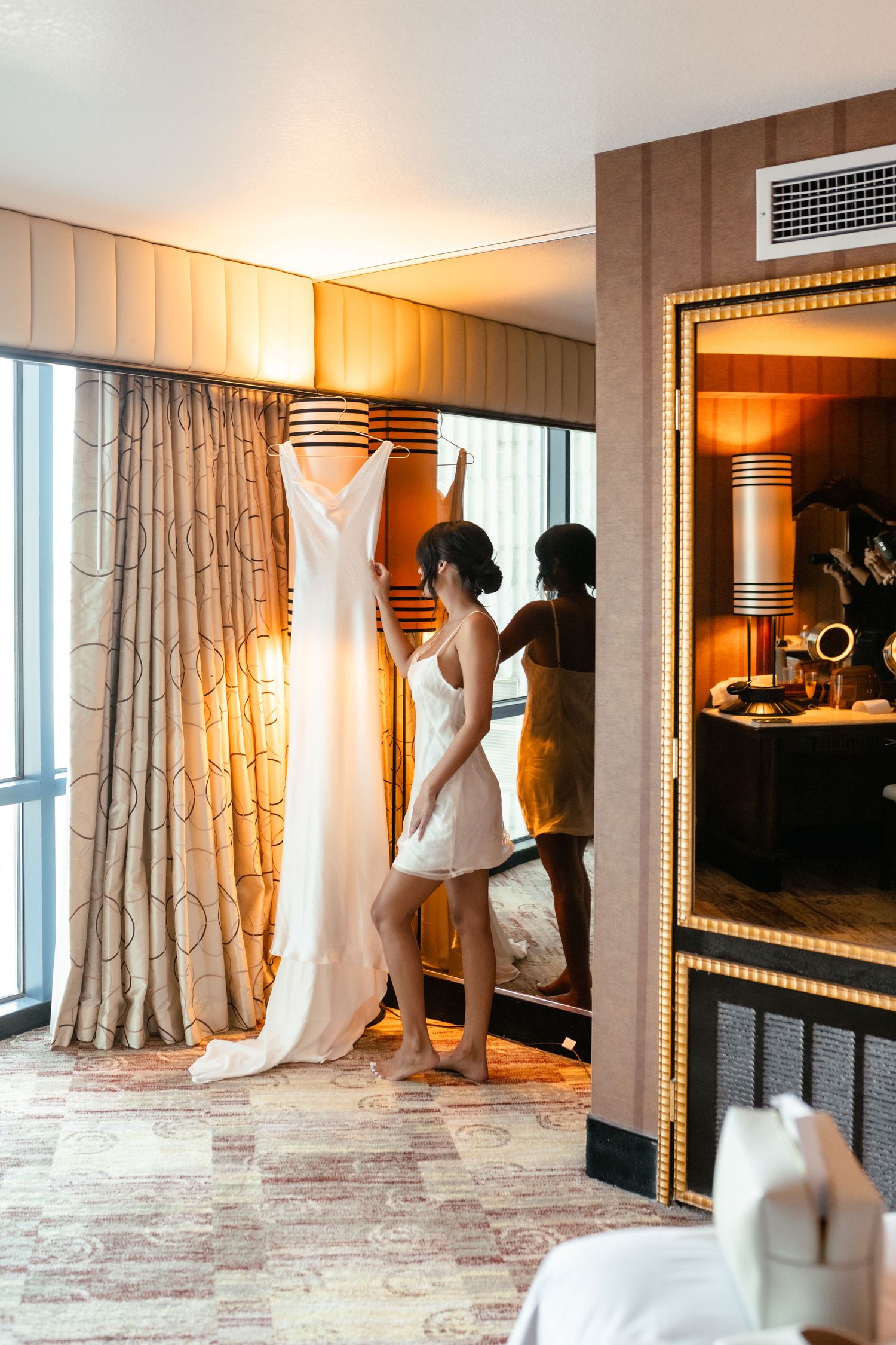 Wedding dress displayed in elegant hotel room with warm lighting and luxurious curtains.