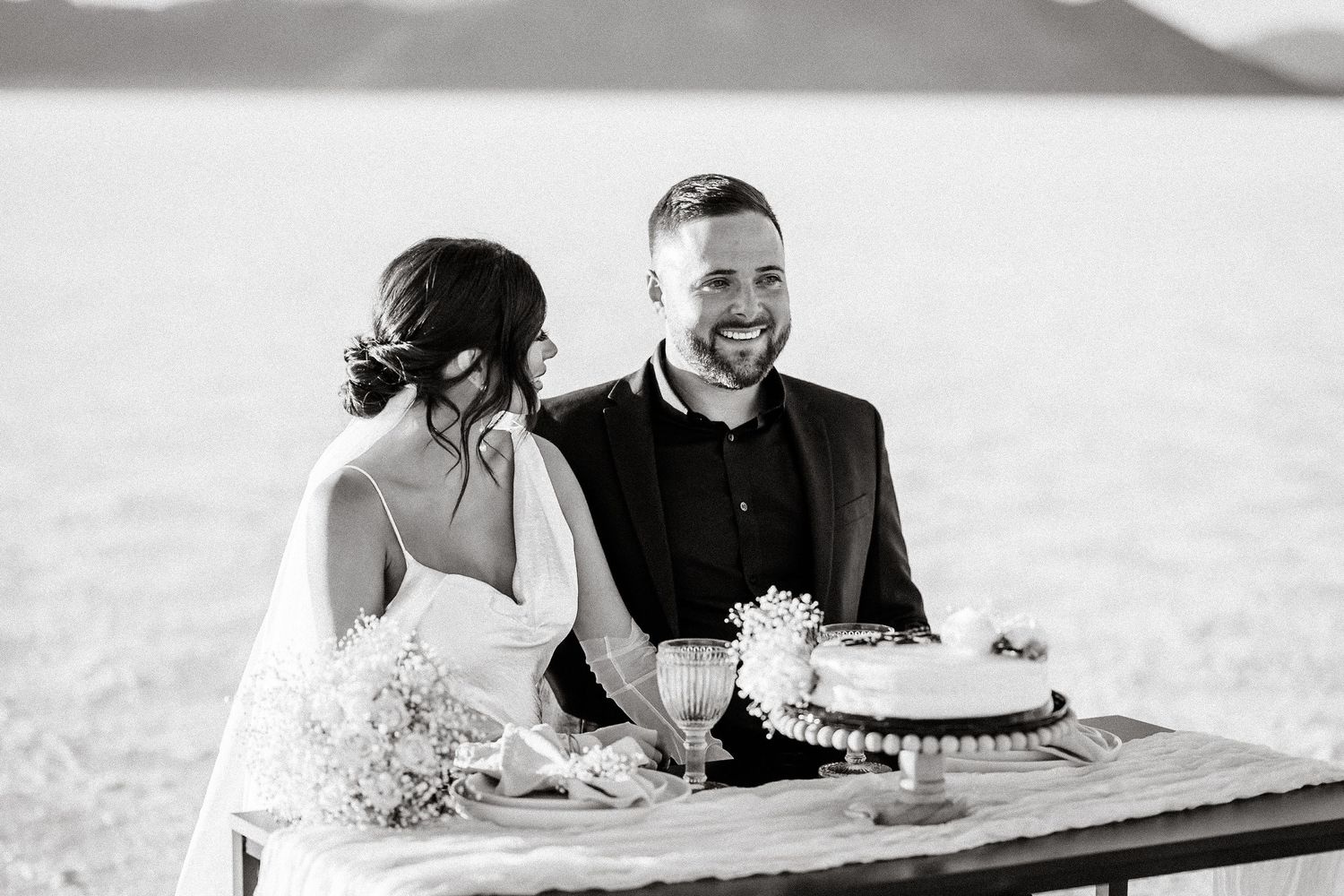 Black and white photo of couple sharing intimate moment at outdoor wedding reception.