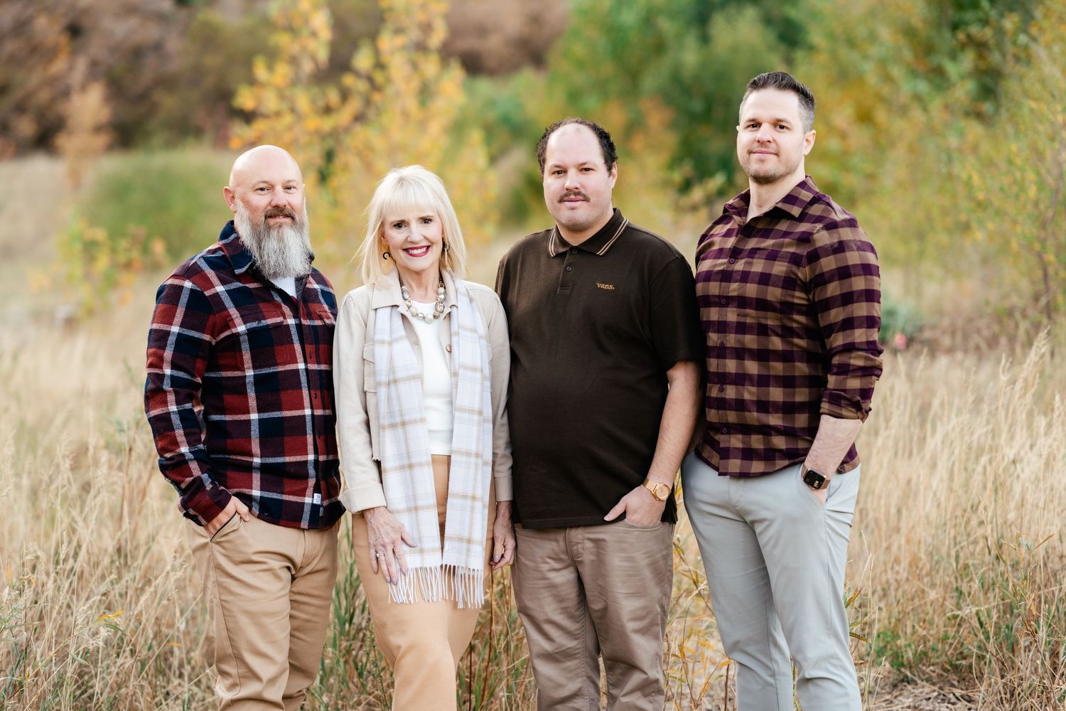 A family group walks together and poses in a grassy field during autumn wearing coordinating plaid and casual outfits.