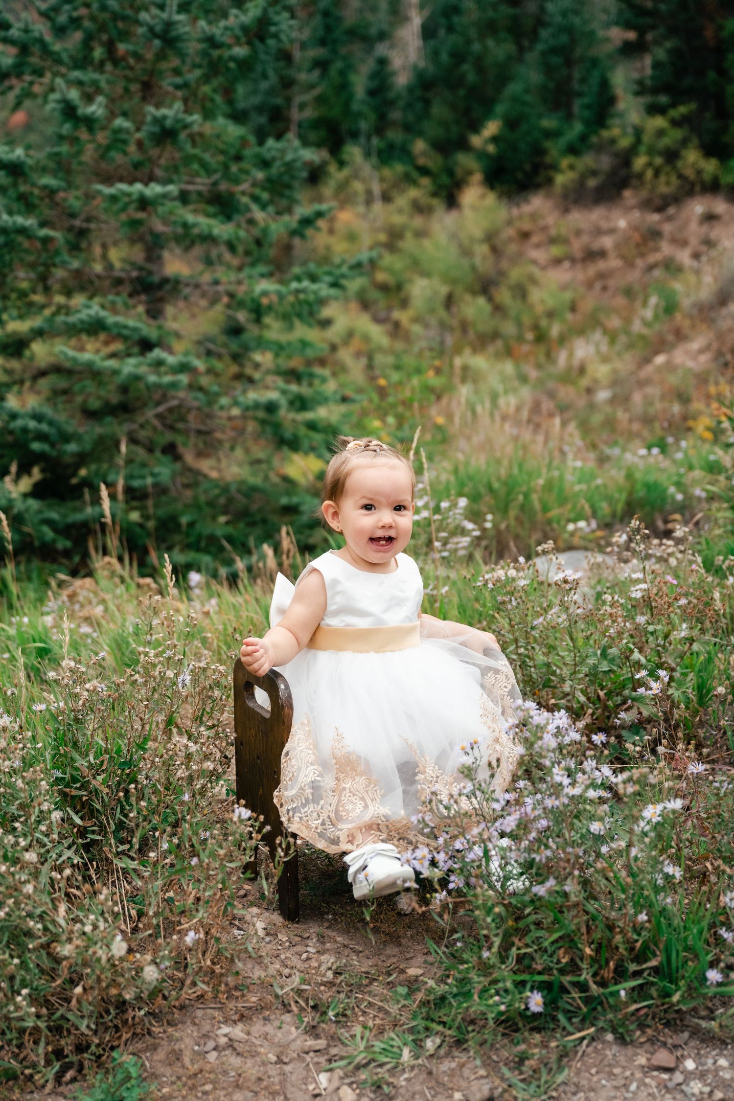 A child in a flowing white dress plays in a meadow surrounded by green foliage.