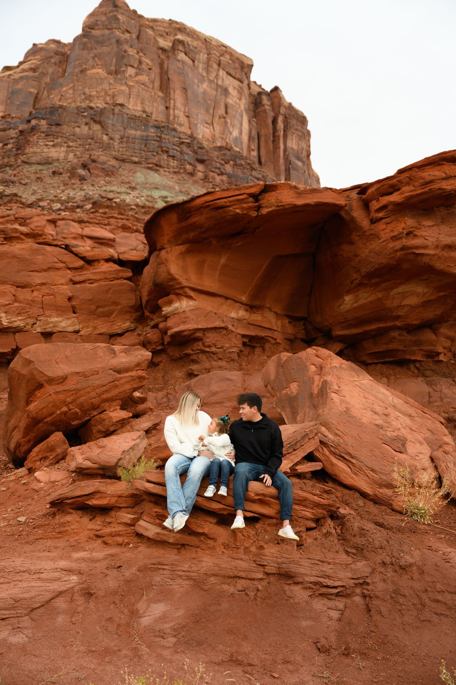 People sitting on red sandstone rock formations at sunset in a desert canyon landscape.