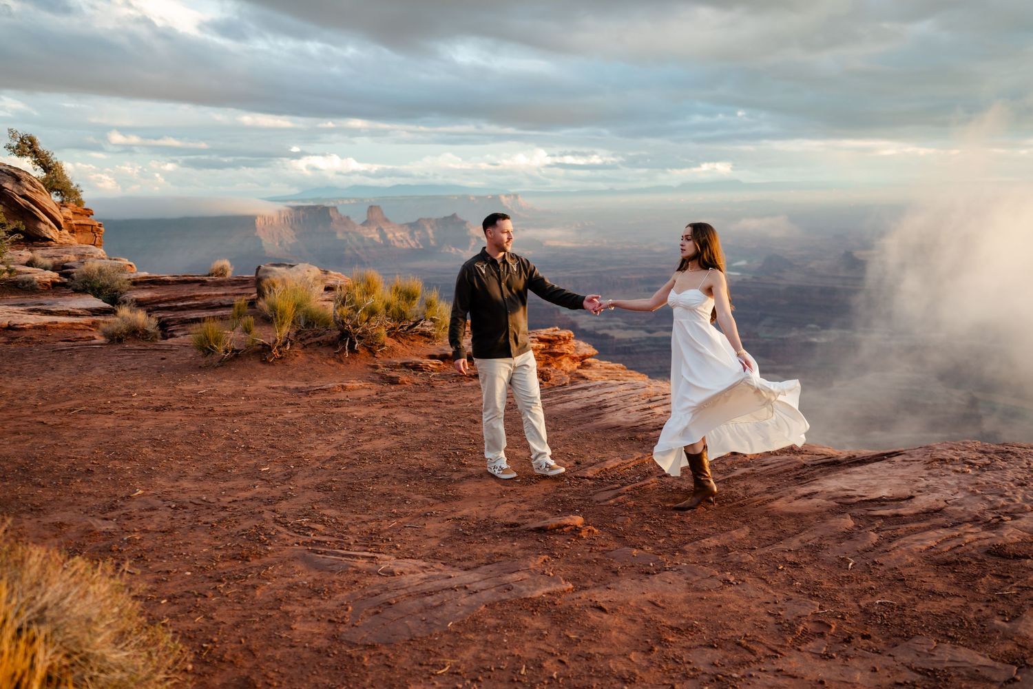 A couple dances together on red rocks overlooking a misty canyon landscape at dusk.