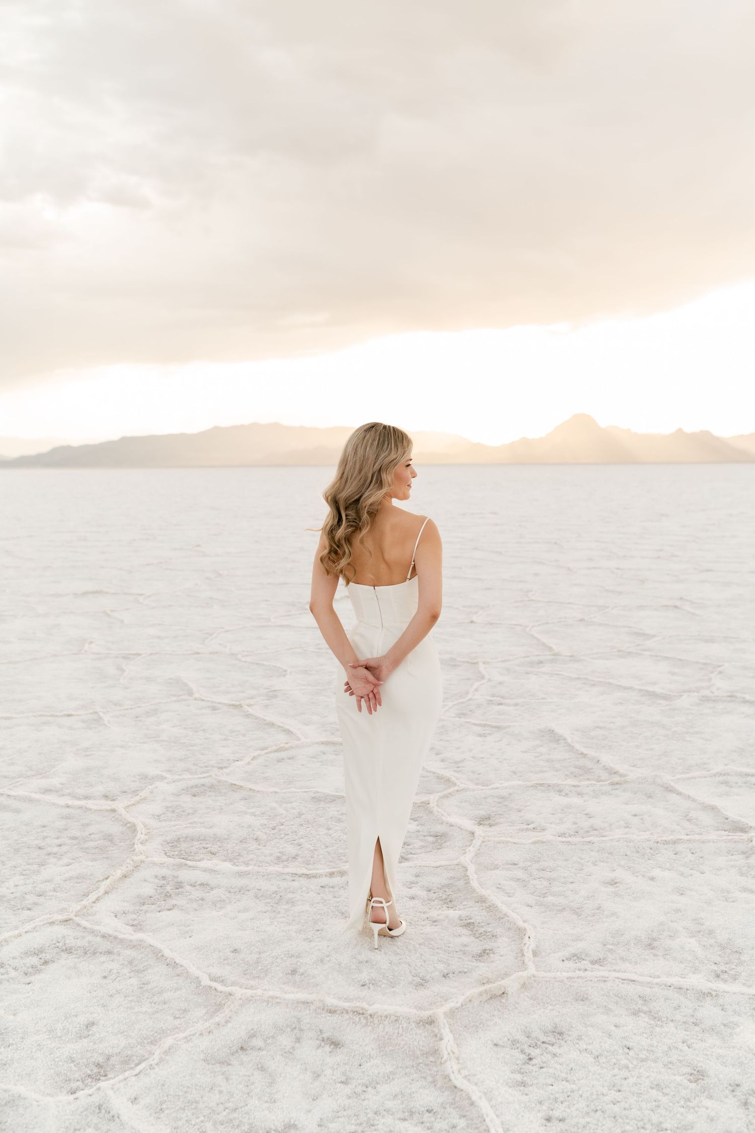 Salt Flats Elopement Photographer. A bride in a white dress walks across a bright salt flat landscape during sunset.