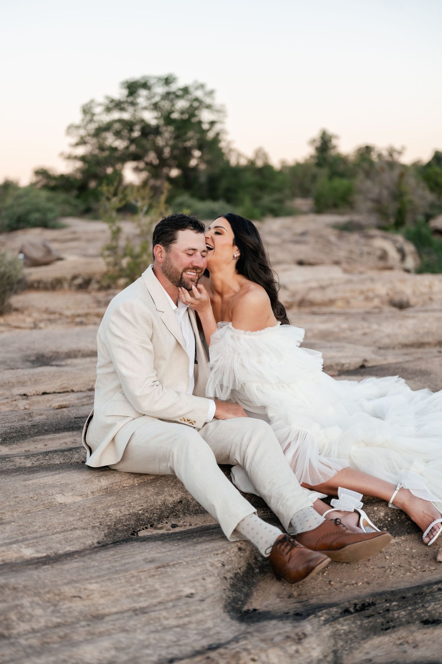 Zion destination photographer. A couple in white attire shares intimate moments on rocky desert terrain during a sunset photoshoot.