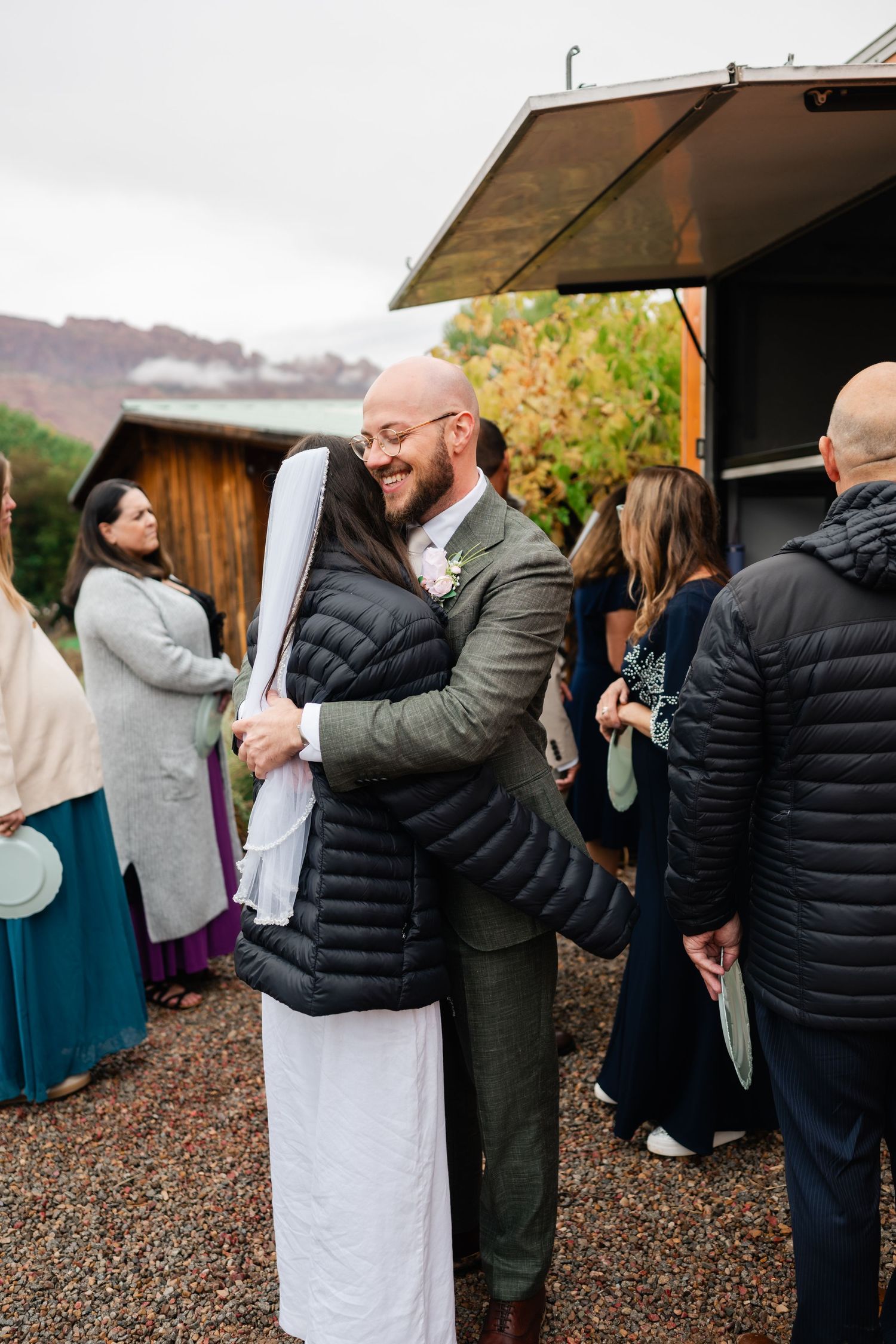 Wedding guests mingling and embracing at an outdoor reception venue.