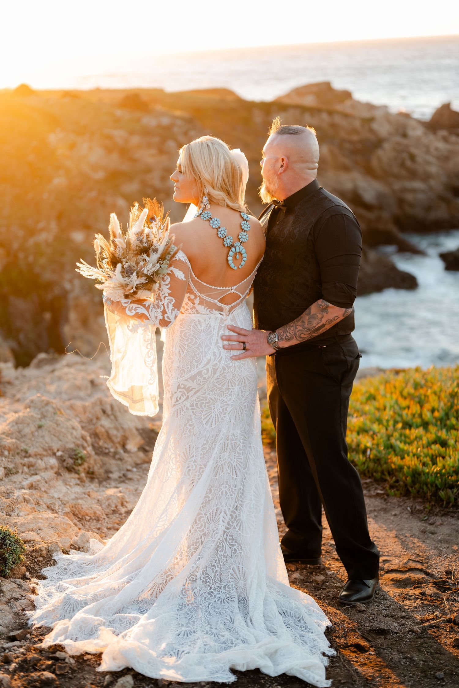 A couple shares an intimate moment on coastal cliffs during sunset in formal wedding attire.