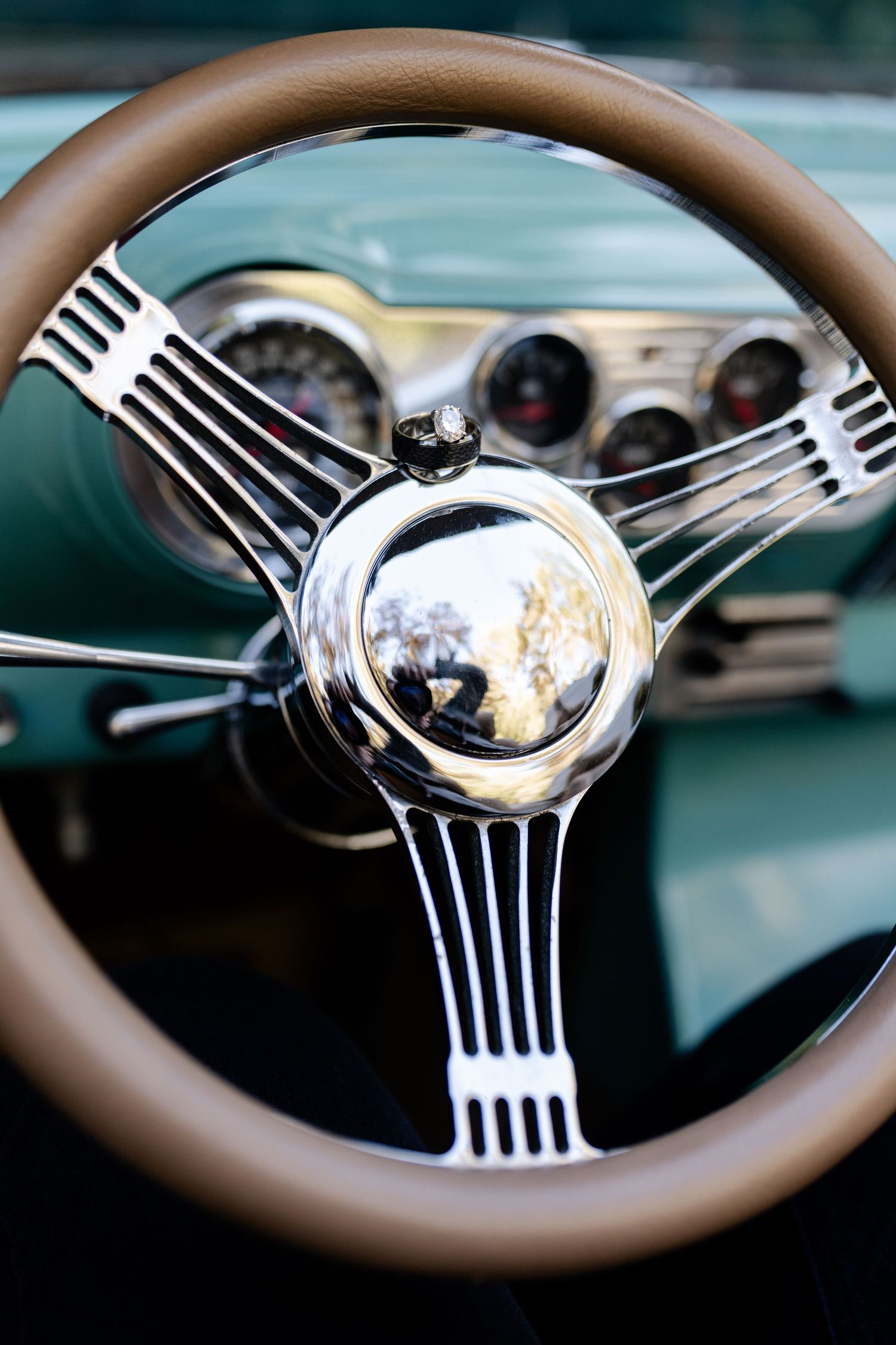 Vintage brown leather steering wheel with chrome details in classic car dashboard.
