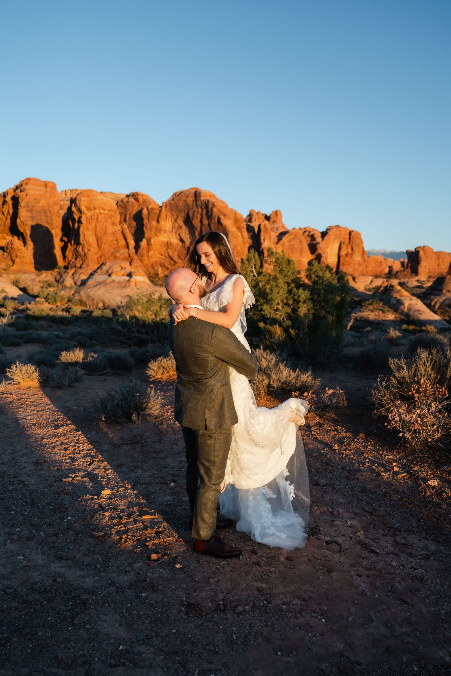 A sunset wedding portrait with dramatic red rock formations in the desert background.