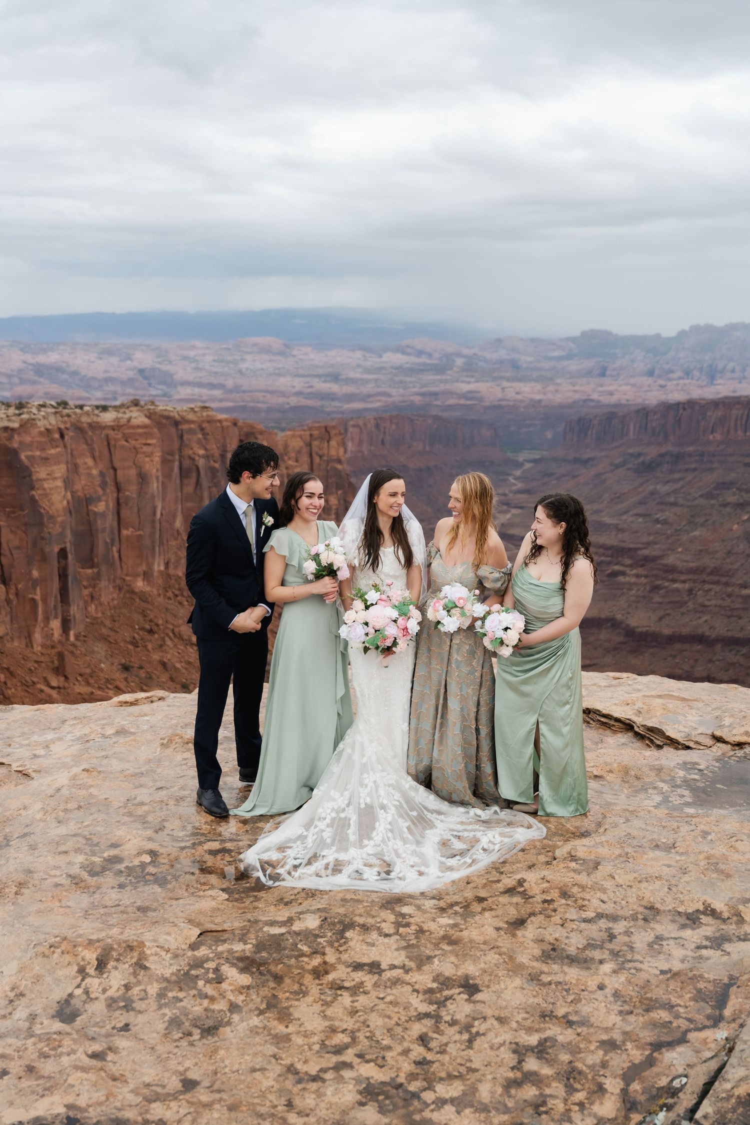 Bridal party in mint green dresses poses together on rocky canyon overlook.